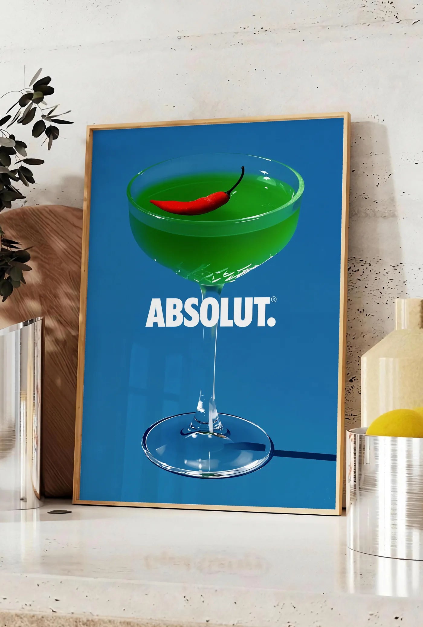 Affiche affiche cocktail vert, posee sur un plan de travail de cuisine en pierre claire, entre une branche d'eucalyptus en vase et un bocal de citrons