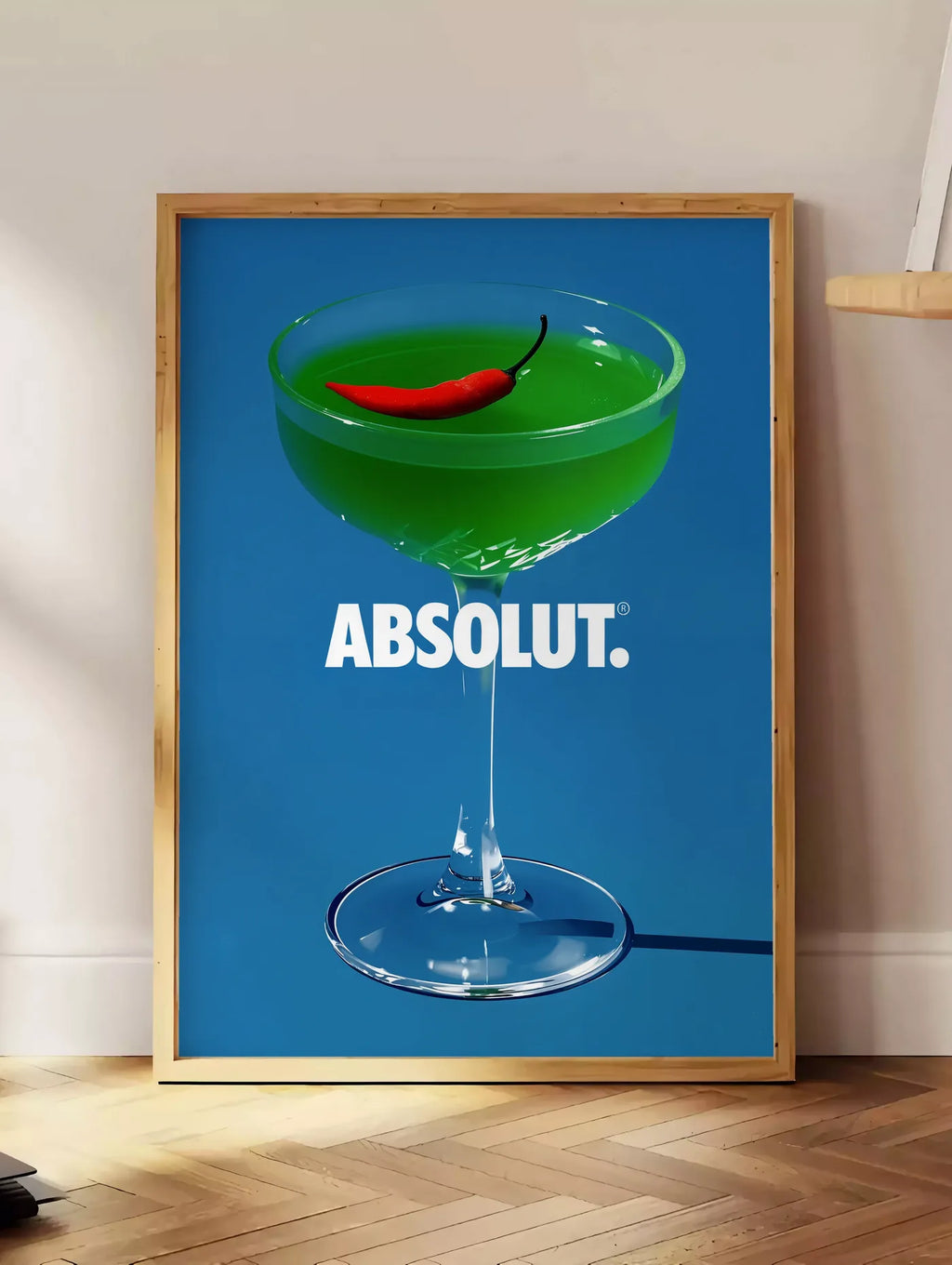 Estampe affiche cocktail vert, posee au sol dans un coin salon, sur un parquet a chevrons, pres d'une table d'appoint en chene chargee de livres
