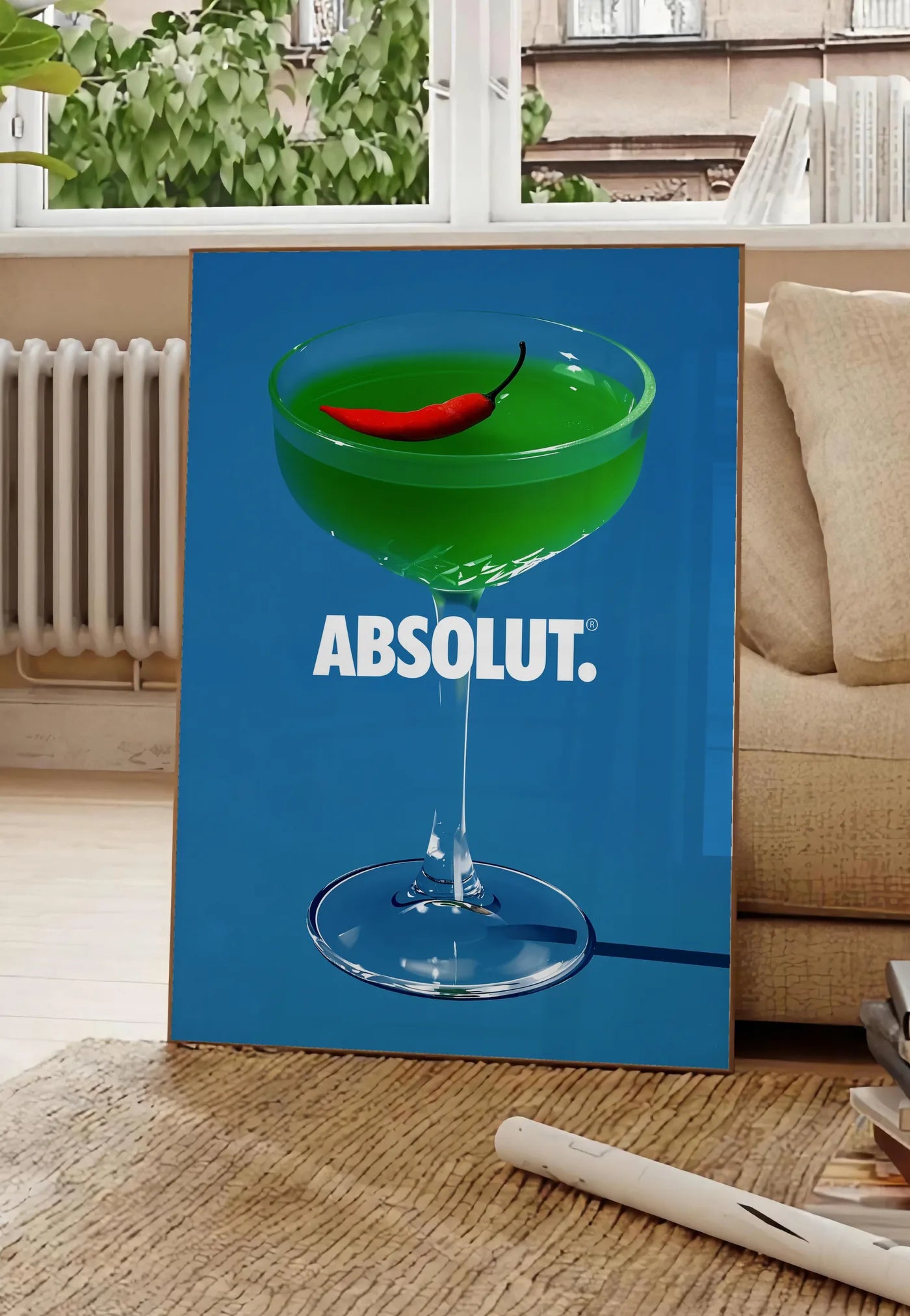 Poster affiche cocktail vert, posee au sol dans un salon parisien, devant une grande fenetre donnant sur un immeuble haussmannien, entre un ficus et un canape creme