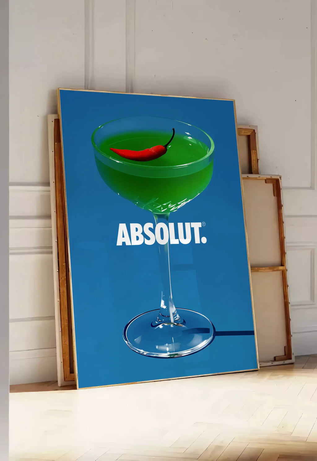 Tirage encadrable affiche cocktail vert, posee au sol dans une entree lumineuse, contre un mur a panneaux blancs, a cote de chassis en bois empiles