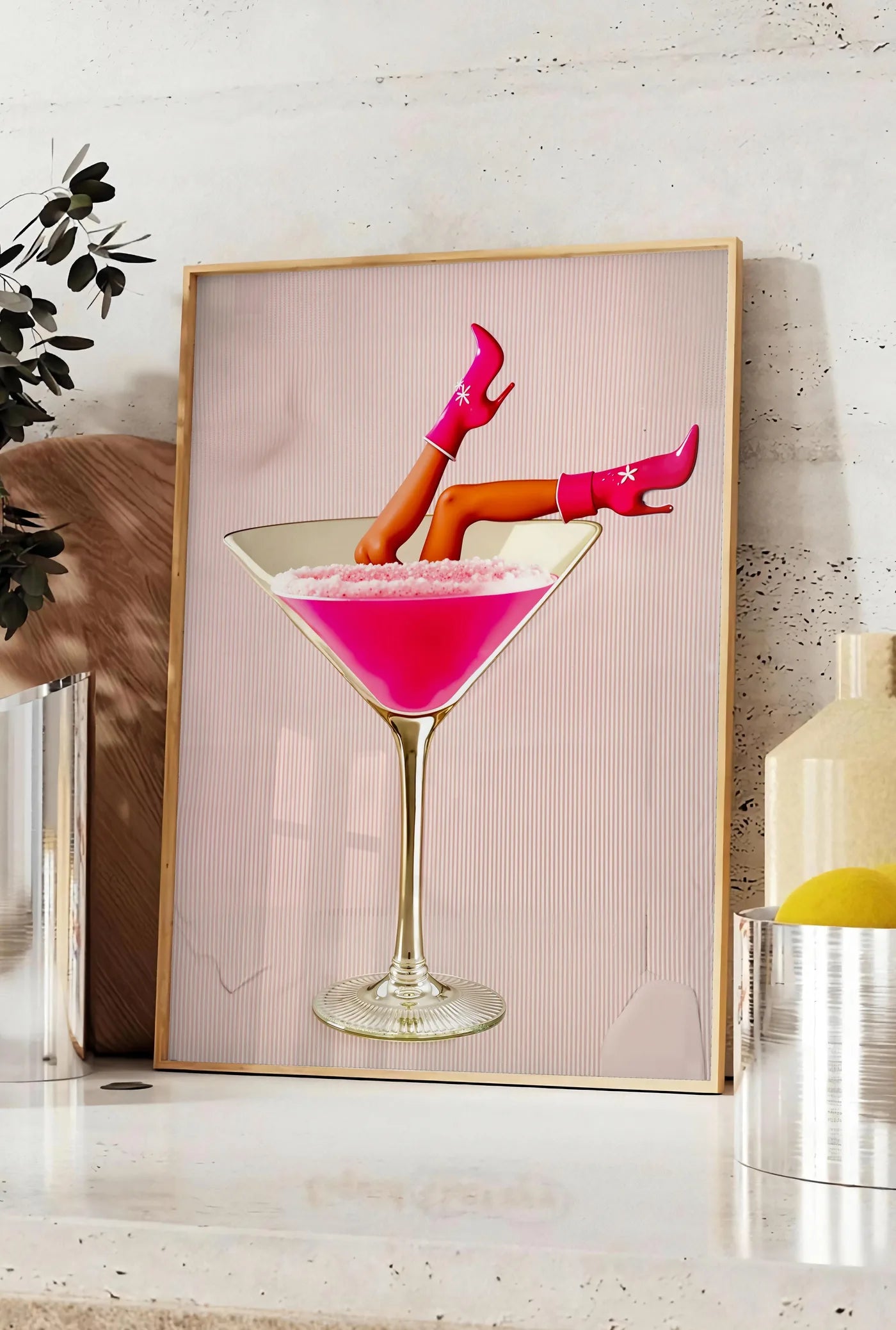 Affiche affiche cocktail rose kitsch, posee sur un plan de travail de cuisine en pierre claire, entre une branche d'eucalyptus en vase et un bocal de citrons