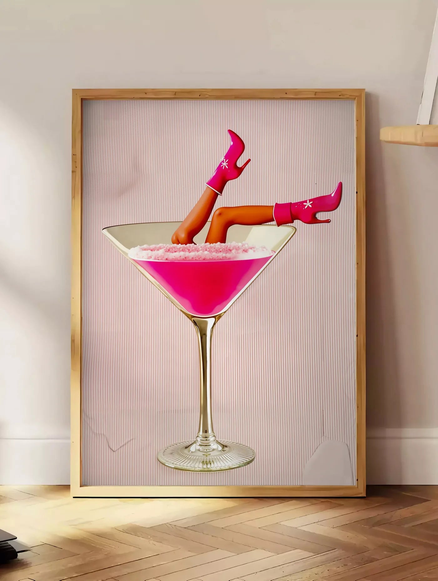 Estampe affiche cocktail rose kitsch, posee au sol dans un coin salon, sur un parquet a chevrons, pres d'une table d'appoint en chene chargee de livres
