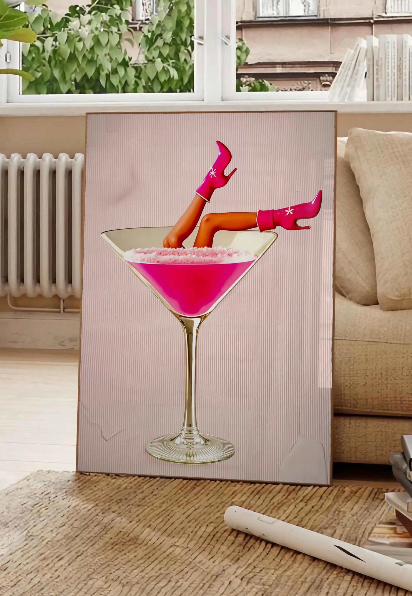 Poster affiche cocktail rose kitsch, posee au sol dans un salon parisien, devant une grande fenetre donnant sur un immeuble haussmannien, entre un ficus et un canape creme