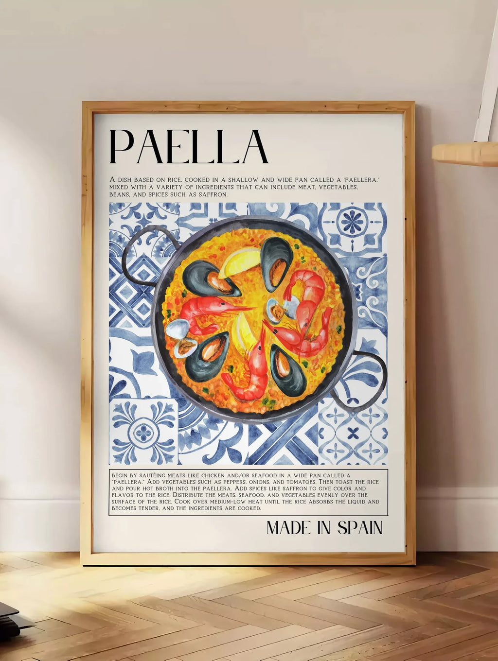 Estampe affiche paella aquarelle, posee au sol dans un coin salon, sur un parquet a chevrons, pres d'une table d'appoint en chene chargee de livres