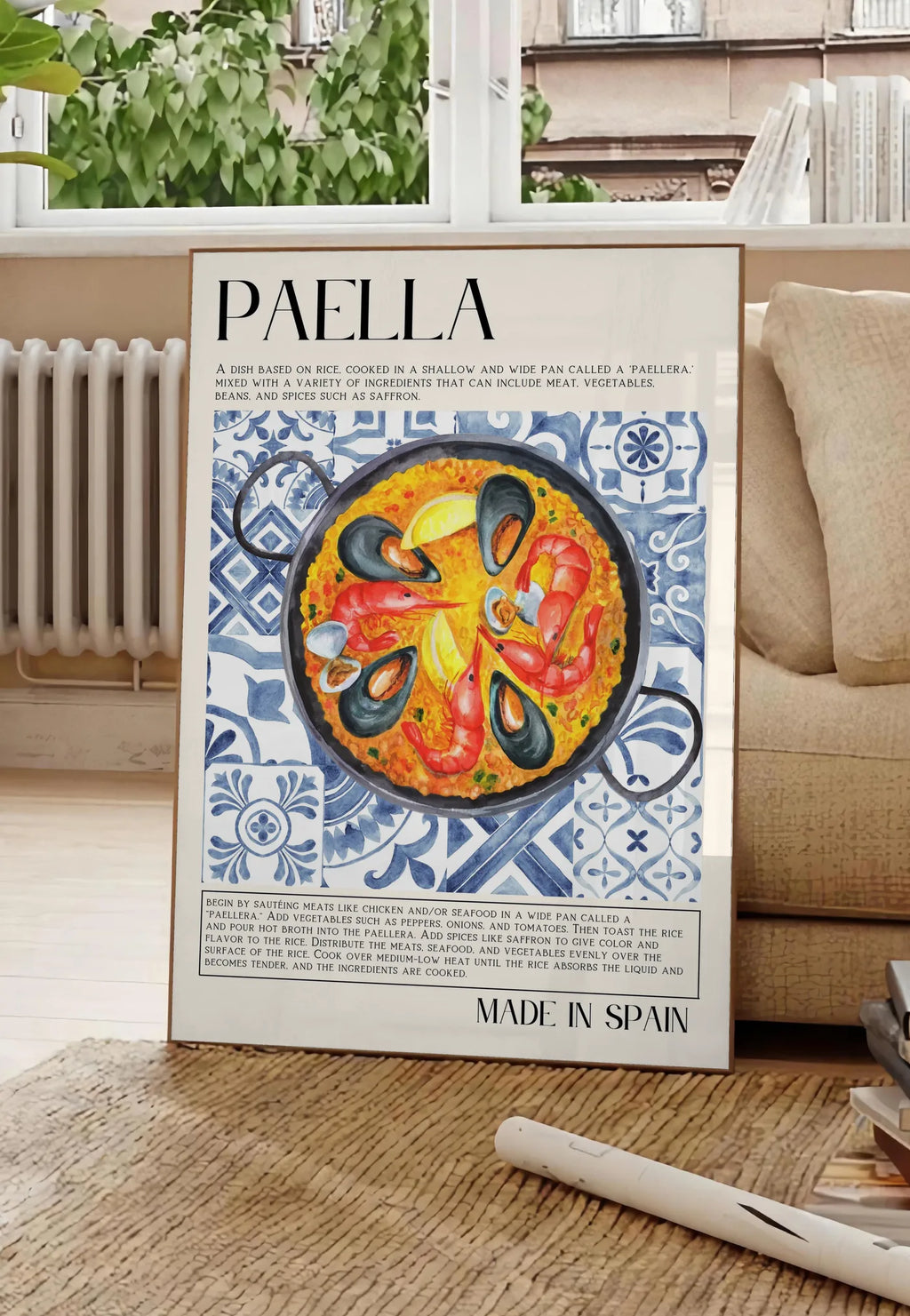 Poster affiche paella aquarelle, posee au sol dans un salon parisien, devant une grande fenetre donnant sur un immeuble haussmannien, entre un ficus et un canape creme