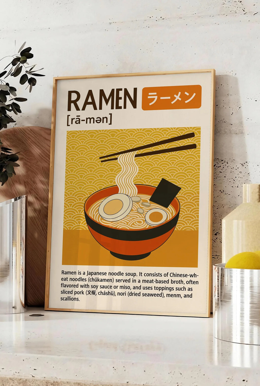 Affiche affiche ramen cuisine, posee sur un plan de travail de cuisine en pierre claire, entre une branche d'eucalyptus en vase et un bocal de citrons