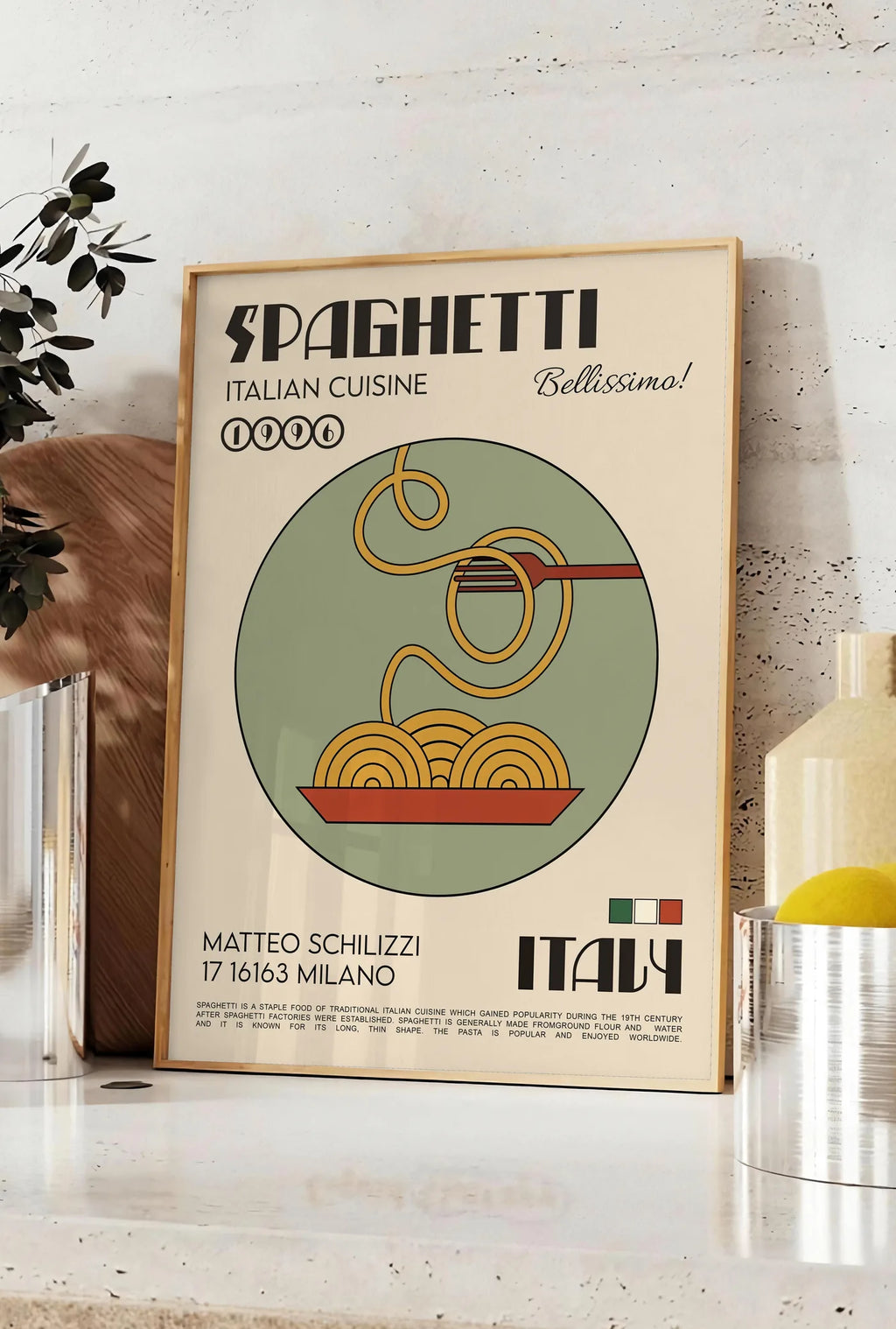 Affiche affiche spaghetti mid-century, posee sur un plan de travail de cuisine en pierre claire, entre une branche d'eucalyptus en vase et un bocal de citrons