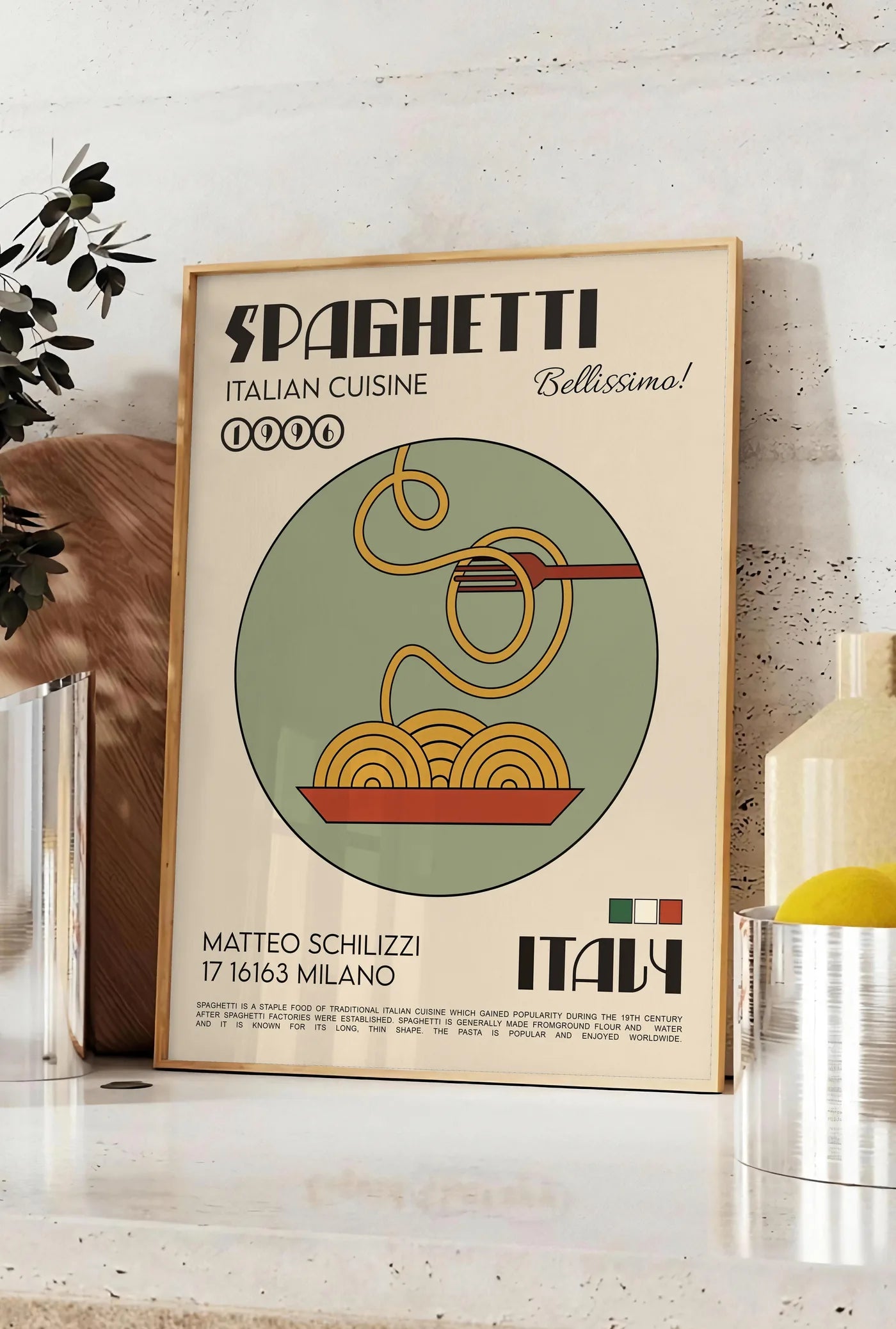 Affiche affiche spaghetti mid-century, posee sur un plan de travail de cuisine en pierre claire, entre une branche d'eucalyptus en vase et un bocal de citrons