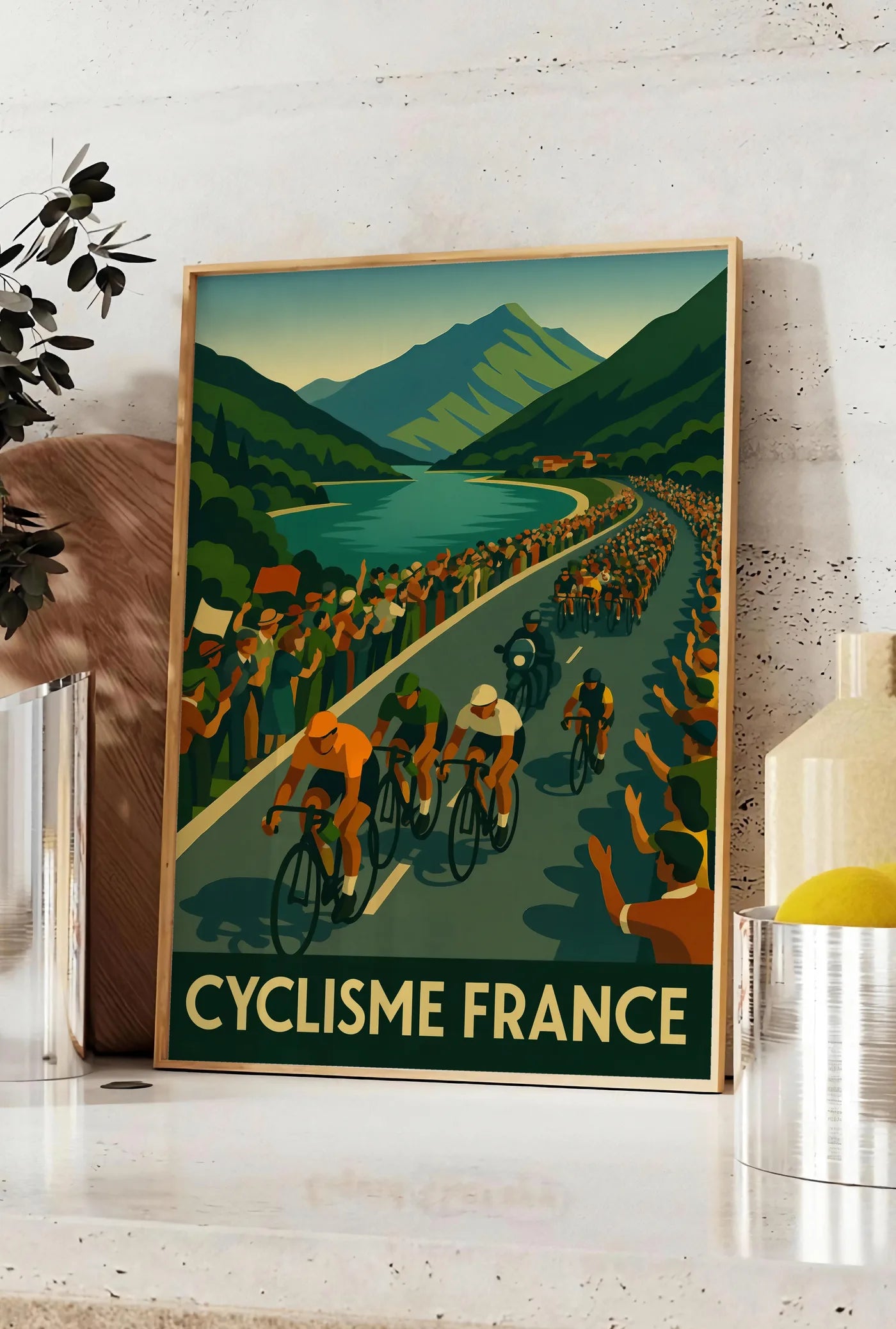 Affiche peloton de cyclistes longe un lac de montagne, posee sur un plan de travail de cuisine en pierre claire, entre une branche d'eucalyptus en vase et un bocal de citrons