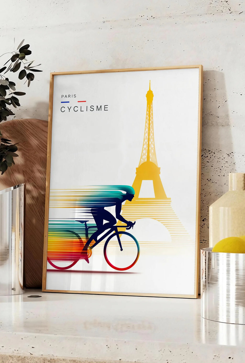 Affiche cycliste stylisé en silhouette filée, posee sur un plan de travail de cuisine en pierre claire, entre une branche d'eucalyptus en vase et un bocal de citrons