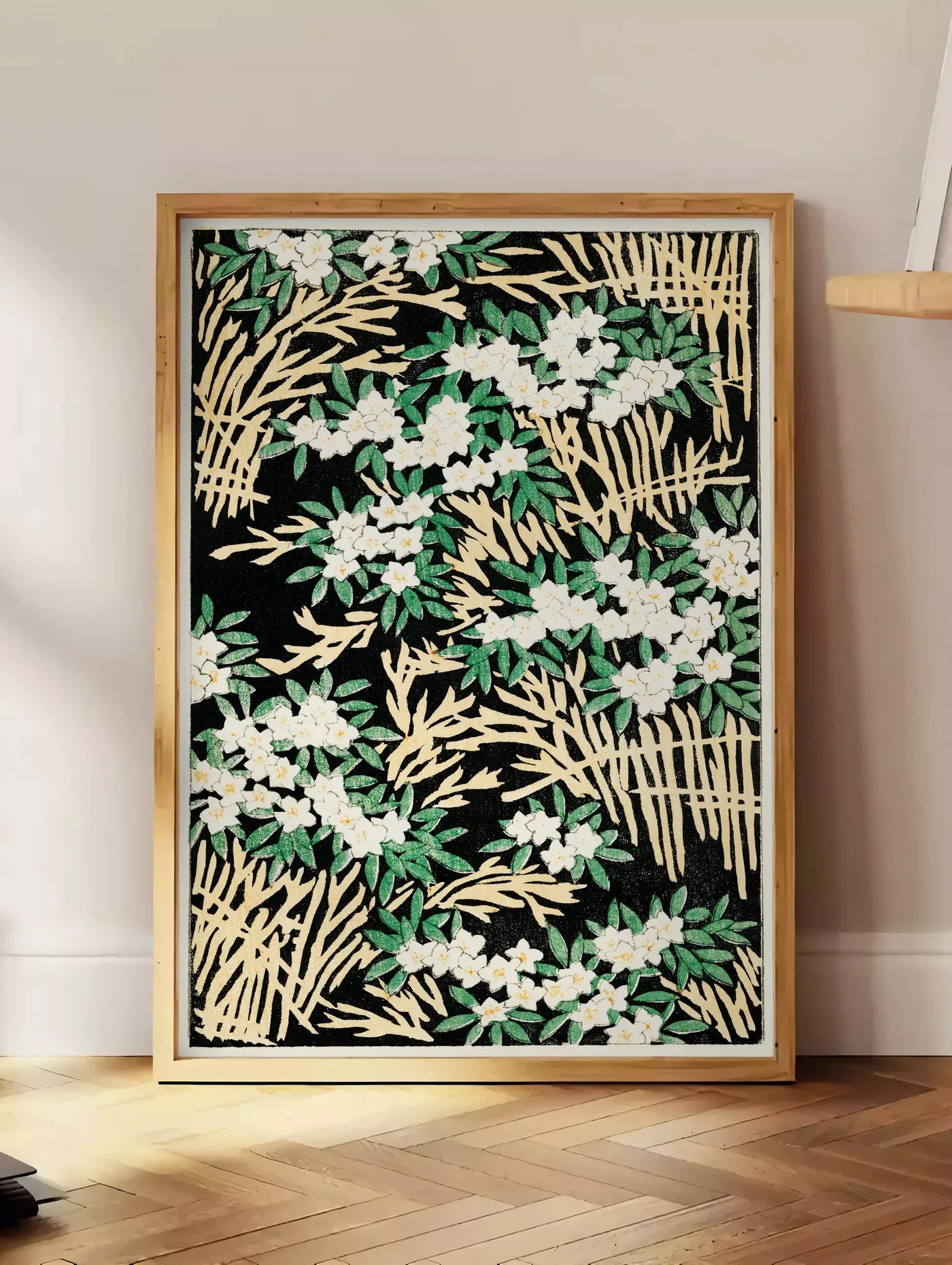 Estampe affiche fleurs blanches sur fond noir art japonais, posee au sol dans un coin salon, sur un parquet a chevrons, pres d'une table d'appoint en chene chargee de livres