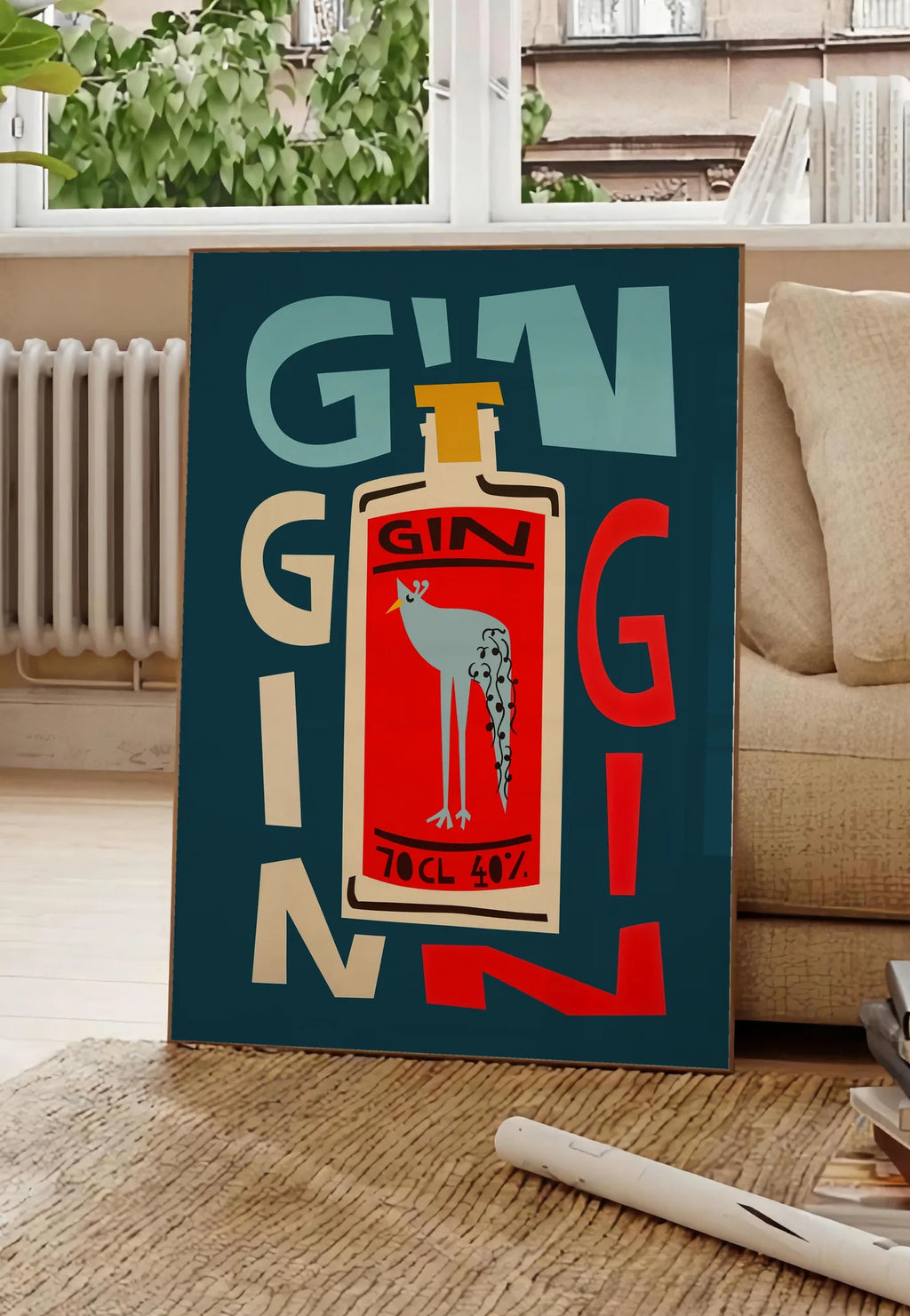 Poster affiche cocktail gin, posee au sol dans un salon parisien, devant une grande fenetre donnant sur un immeuble haussmannien, entre un ficus et un canape creme