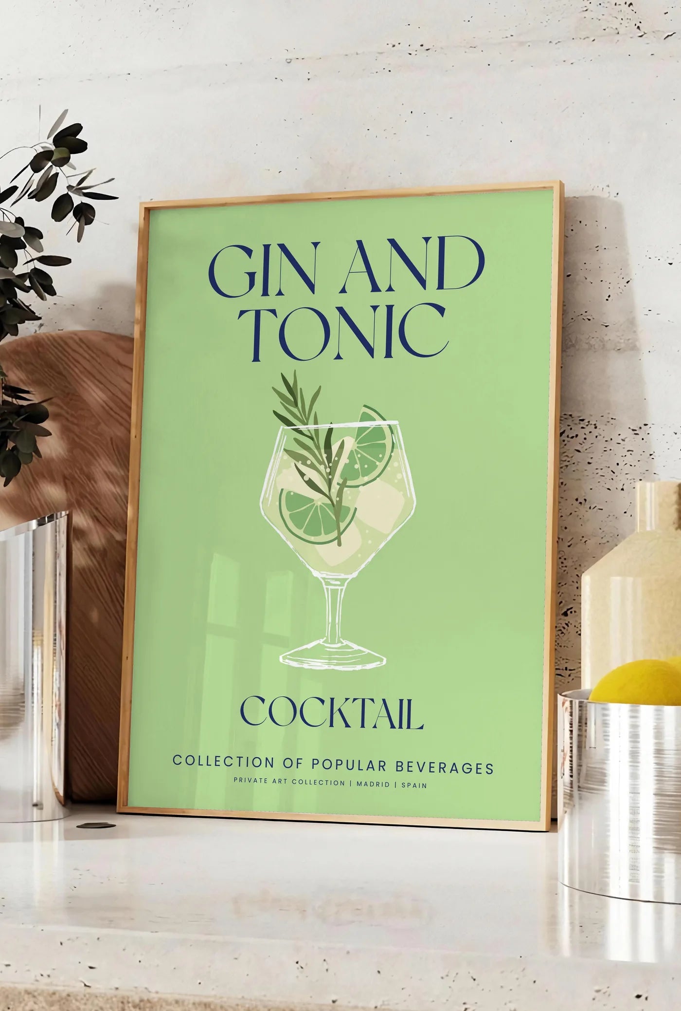 Affiche affiche cocktail Gin Tonic, posee sur un plan de travail de cuisine en pierre claire, entre une branche d'eucalyptus en vase et un bocal de citrons