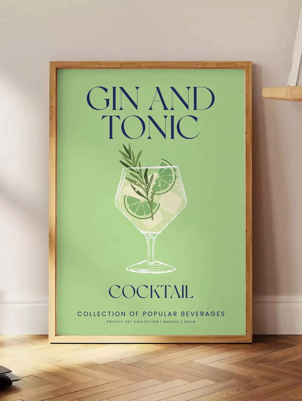Estampe affiche cocktail Gin Tonic, posee au sol dans un coin salon, sur un parquet a chevrons, pres d'une table d'appoint en chene chargee de livres