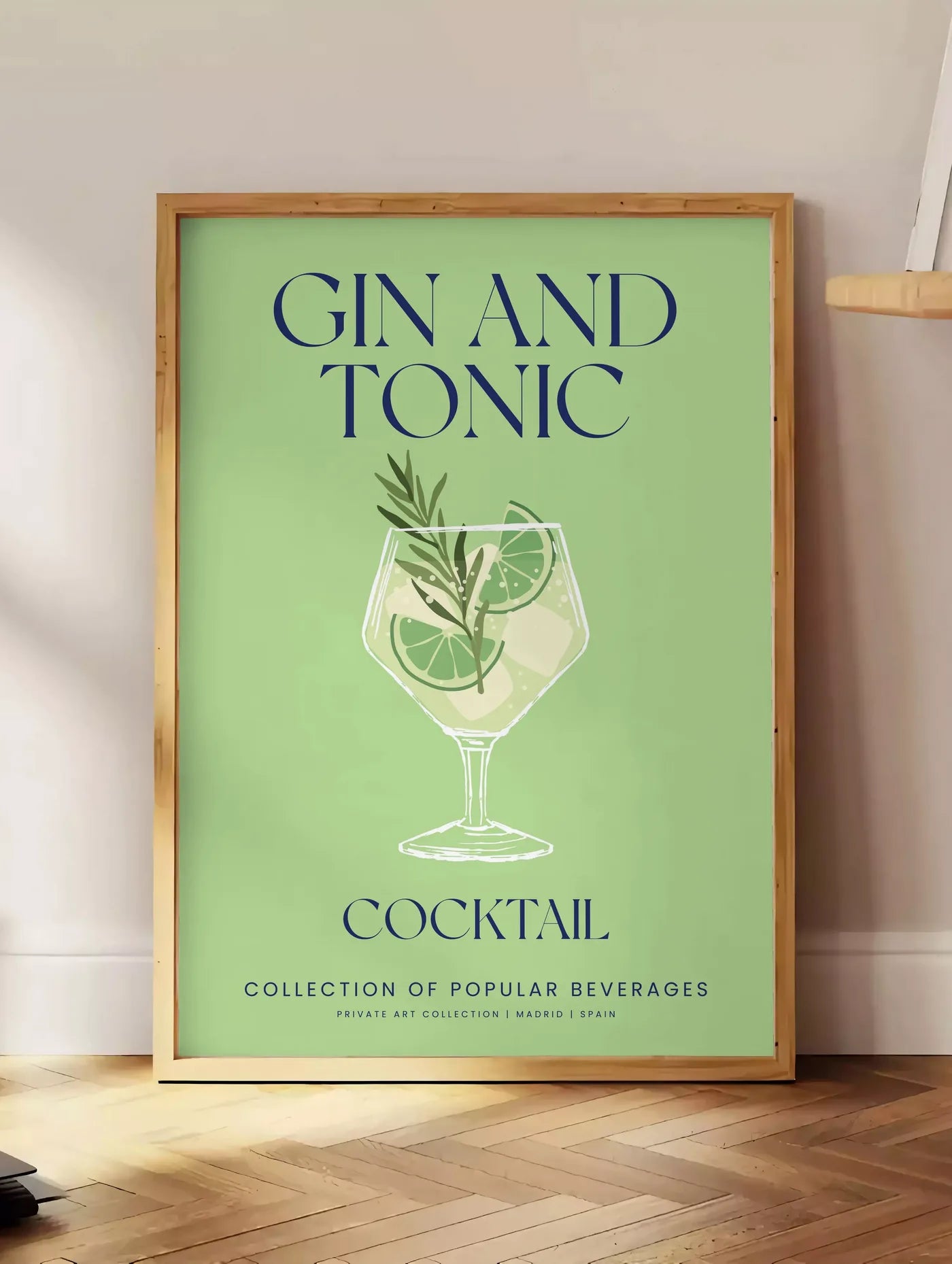 Estampe affiche cocktail Gin Tonic, posee au sol dans un coin salon, sur un parquet a chevrons, pres d'une table d'appoint en chene chargee de livres