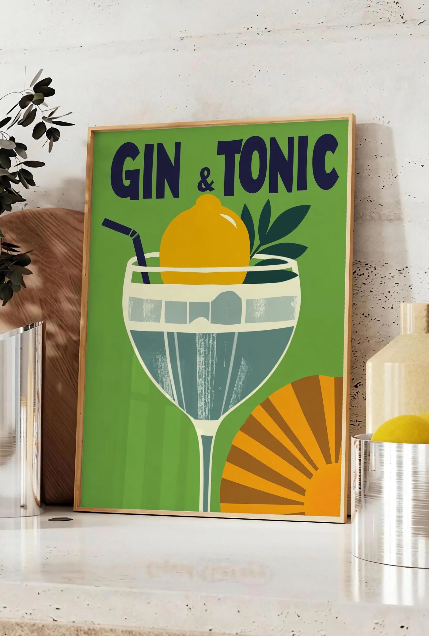 Affiche affiche cocktail Gin Tonic, posee sur un plan de travail de cuisine en pierre claire, entre une branche d'eucalyptus en vase et un bocal de citrons