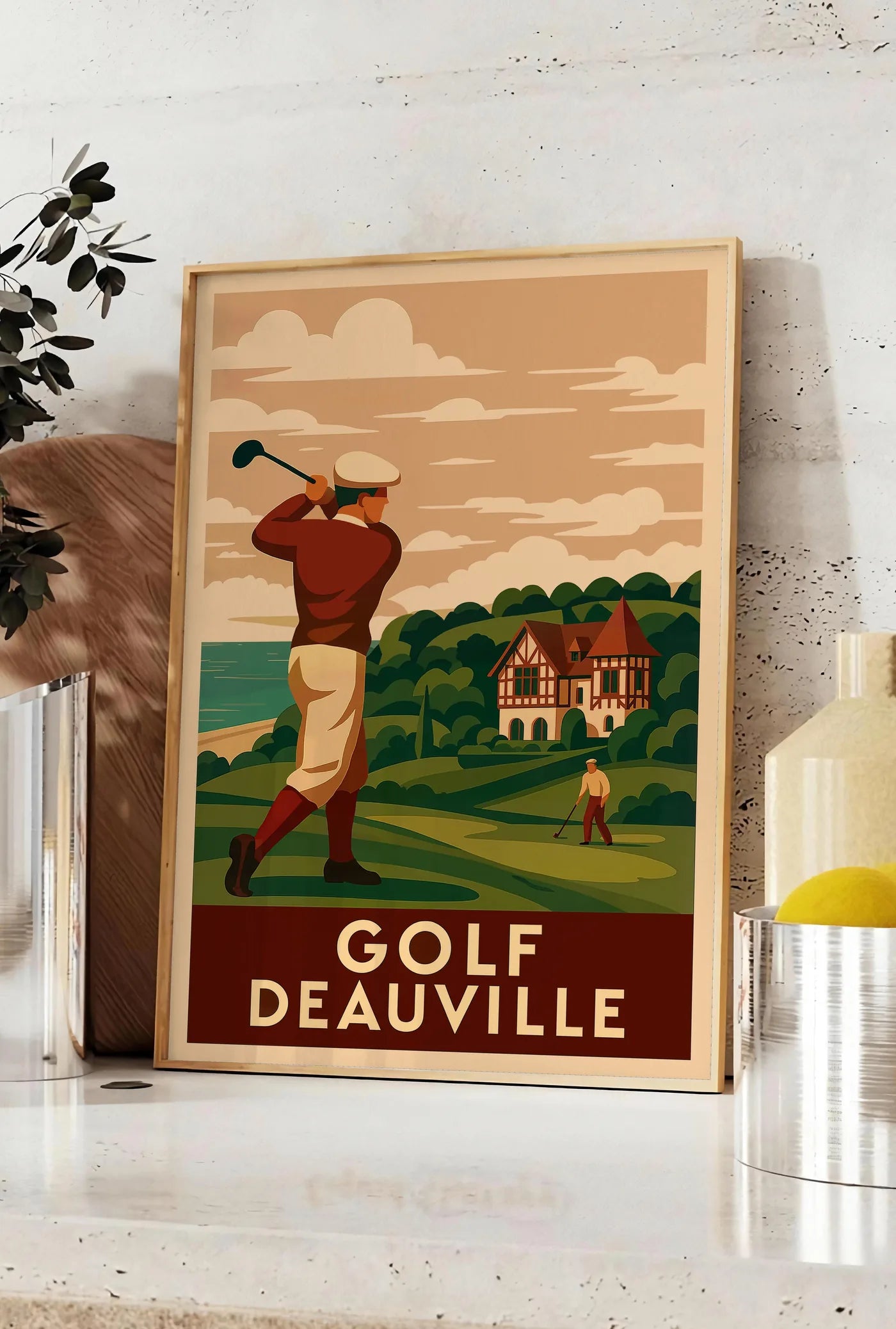 Affiche golfeur en swing face à la mer, posee sur un plan de travail de cuisine en pierre claire, entre une branche d'eucalyptus en vase et un bocal de citrons