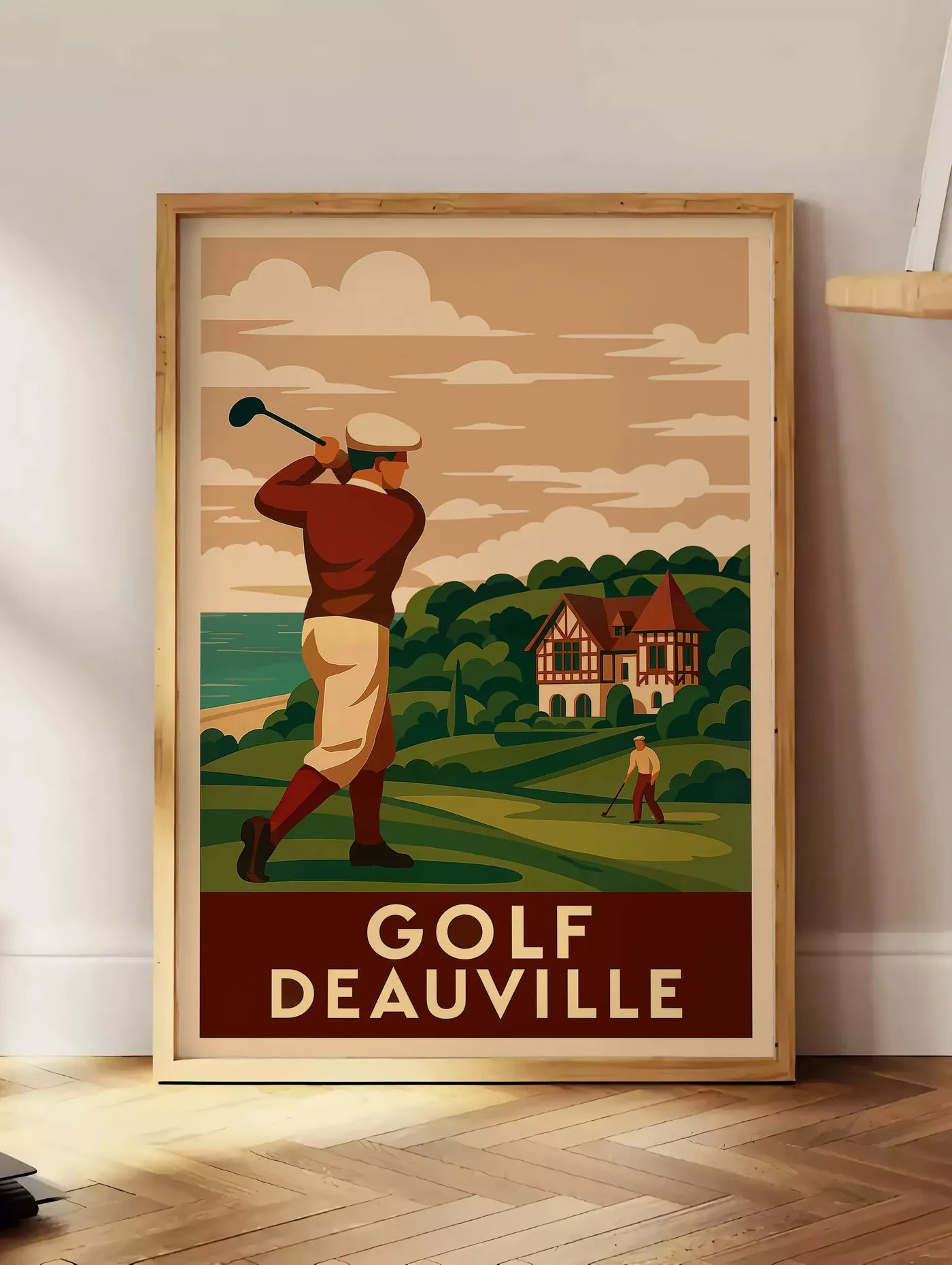 Estampe golfeur en swing face à la mer, posee au sol dans un coin salon, sur un parquet a chevrons, pres d'une table d'appoint en chene chargee de livres
