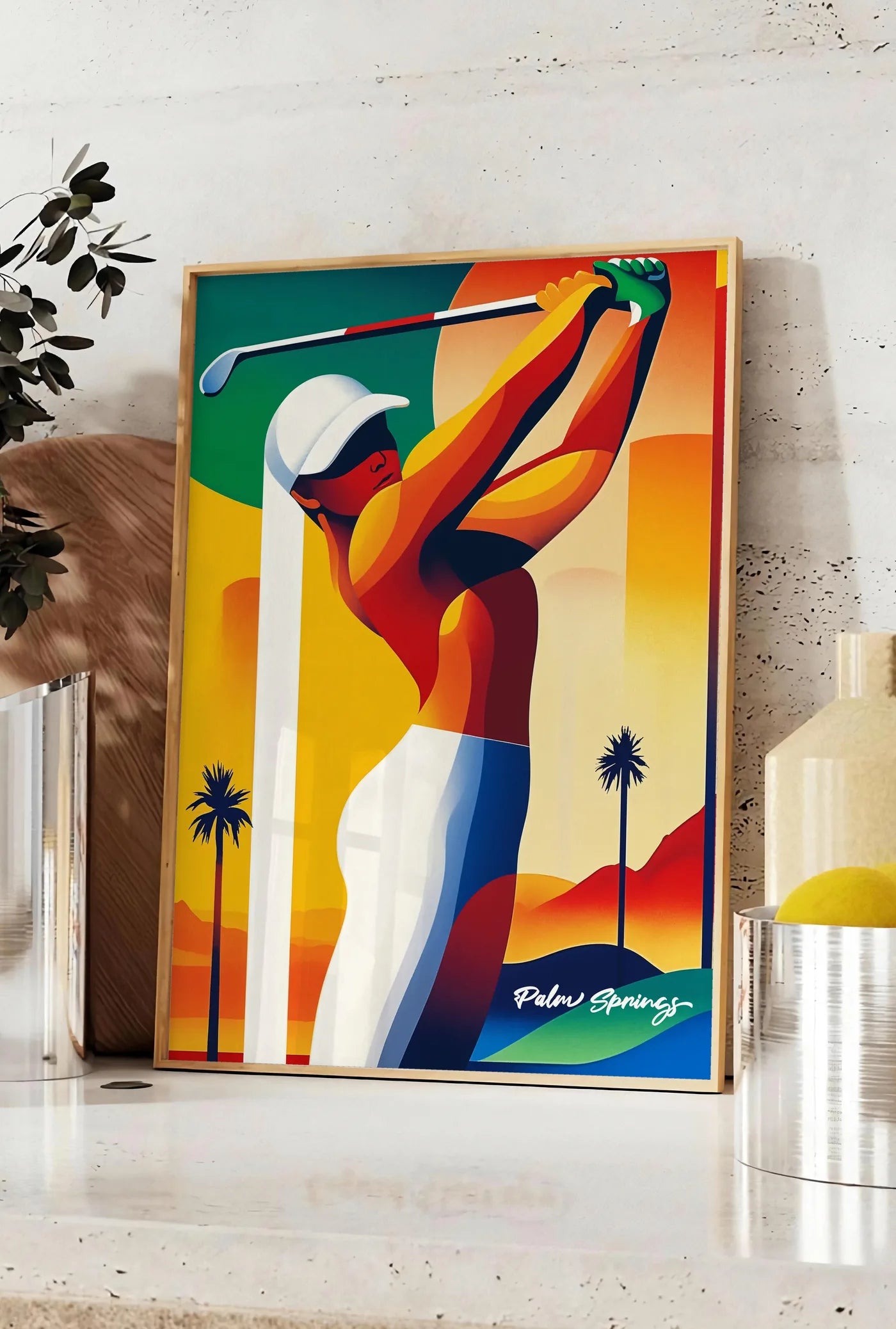 Affiche golfeuse stylisée effectue un swing, posee sur un plan de travail de cuisine en pierre claire, entre une branche d'eucalyptus en vase et un bocal de citrons