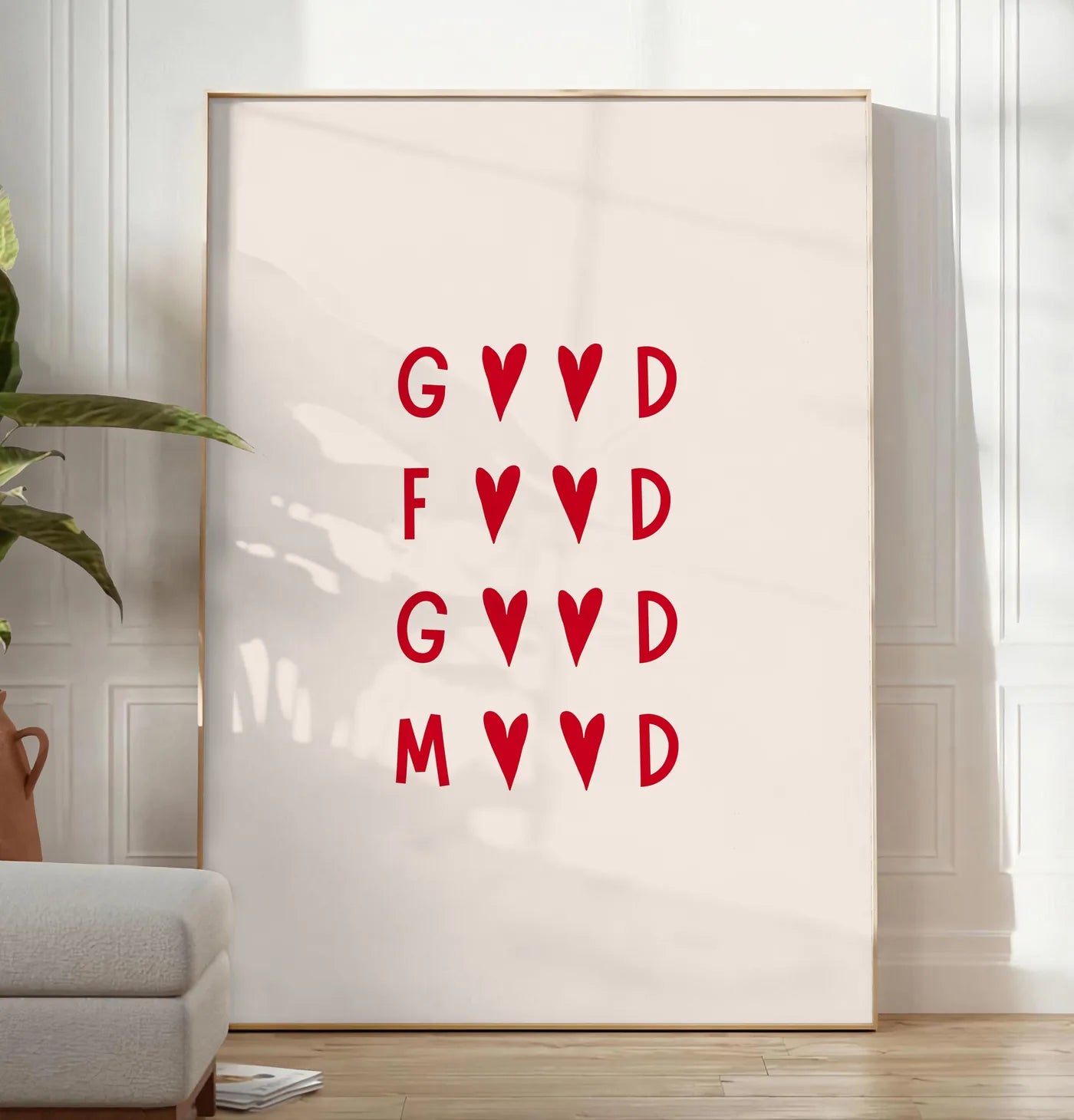 Reproduction affiche cuisine Good Food Good Mood, posee au sol dans un salon minimaliste clair, a cote d'un canape beige et d'une plante verte, sur un parquet clair
