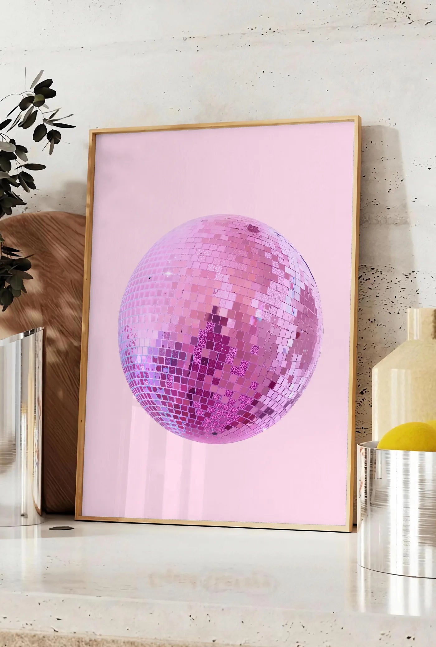 Affiche affiche vintage boule disco rose a facettes sur fond rose poudre, posee sur un plan de travail de cuisine en pierre claire, entre une branche d'eucalyptus en vase et un bocal de citrons