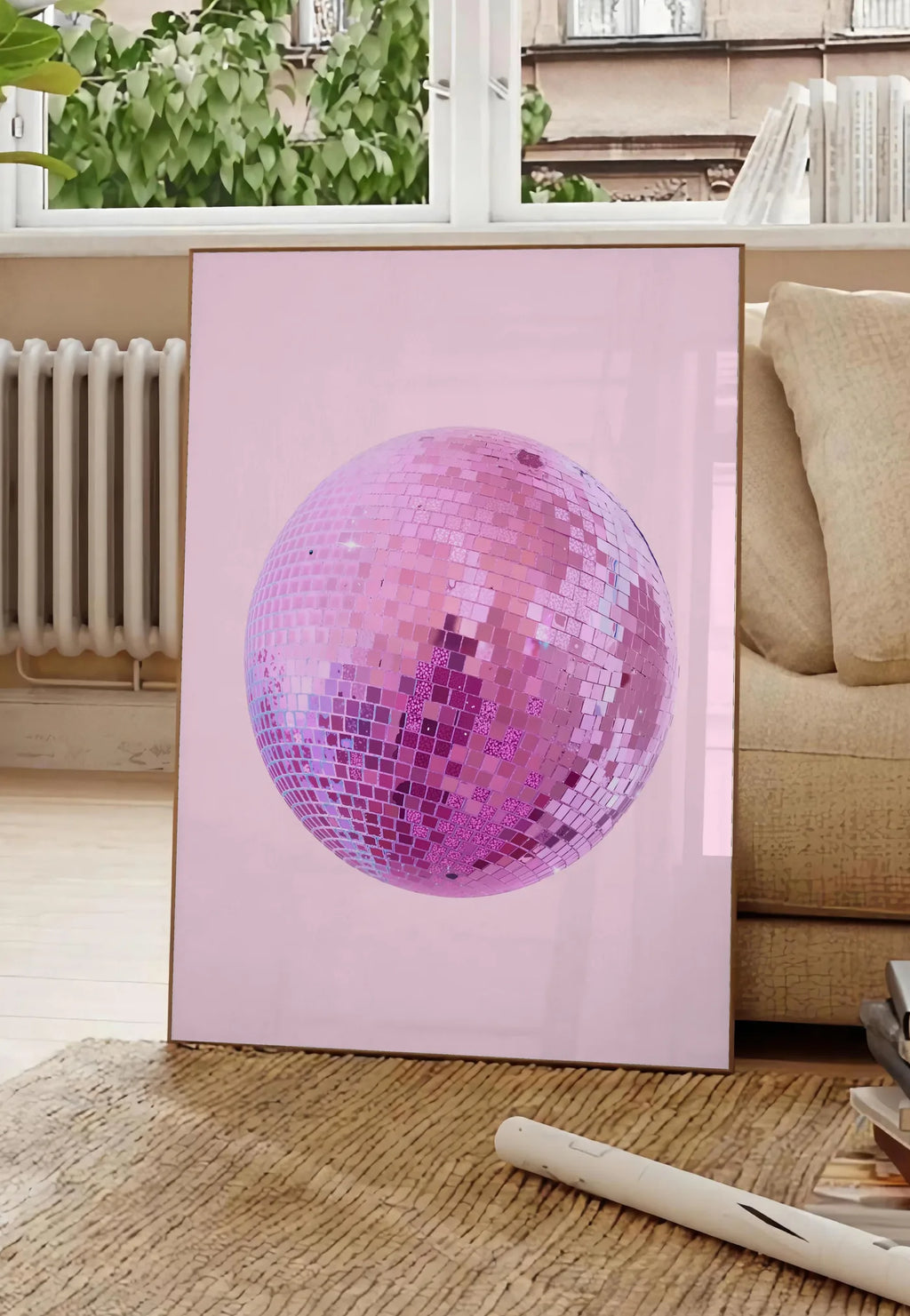 Poster affiche vintage boule disco rose a facettes sur fond rose poudre, posee au sol dans un salon parisien, devant une grande fenetre donnant sur un immeuble haussmannien, entre un ficus et un canape creme