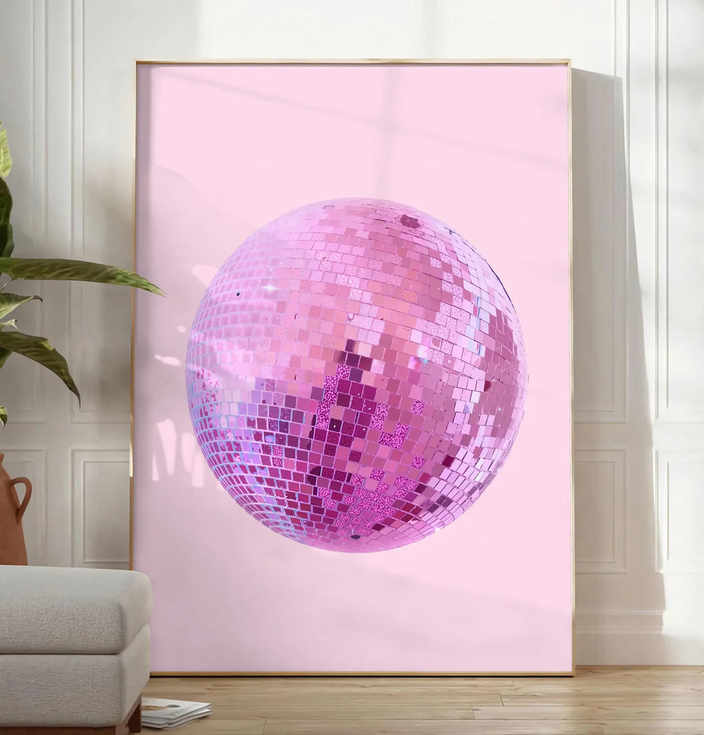 Reproduction affiche vintage boule disco rose a facettes sur fond rose poudre, posee au sol dans un salon minimaliste clair, a cote d'un canape beige et d'une plante verte, sur un parquet clair