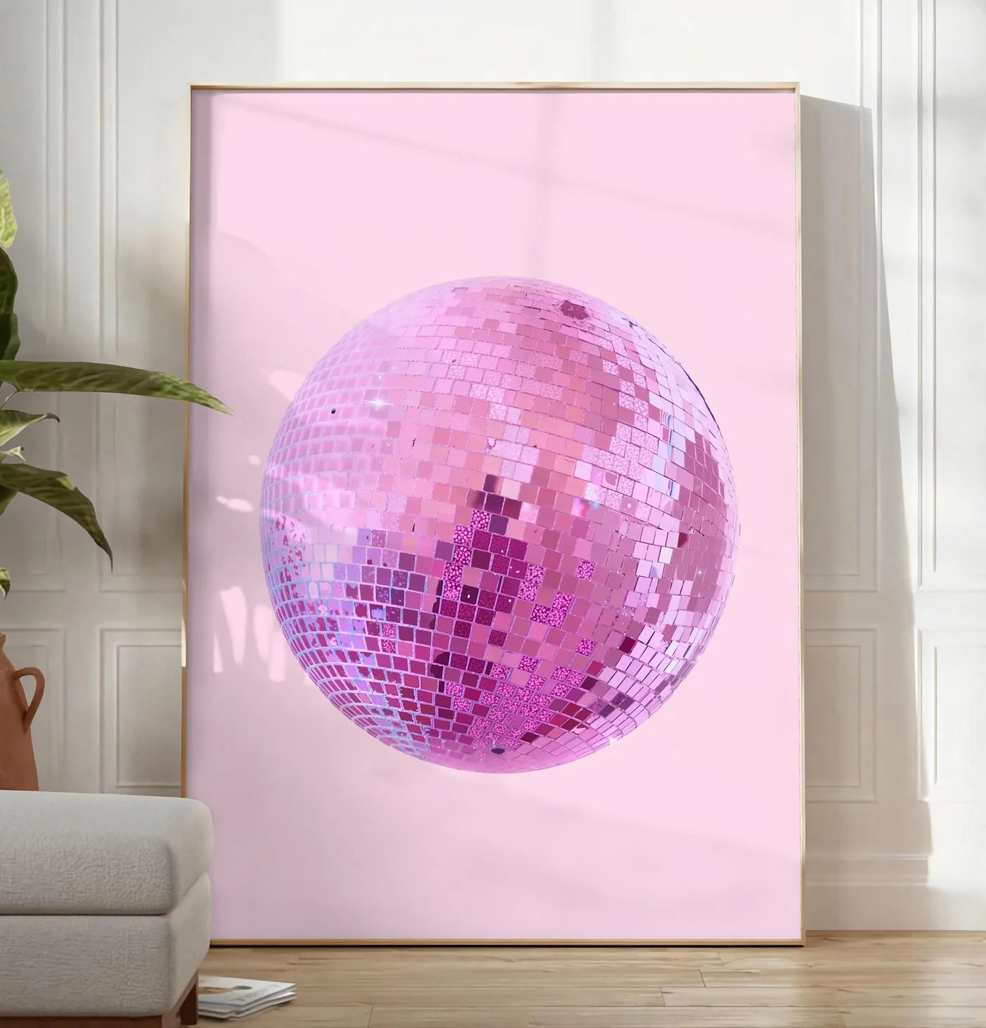 Reproduction affiche vintage boule disco rose a facettes sur fond rose poudre, posee au sol dans un salon minimaliste clair, a cote d'un canape beige et d'une plante verte, sur un parquet clair