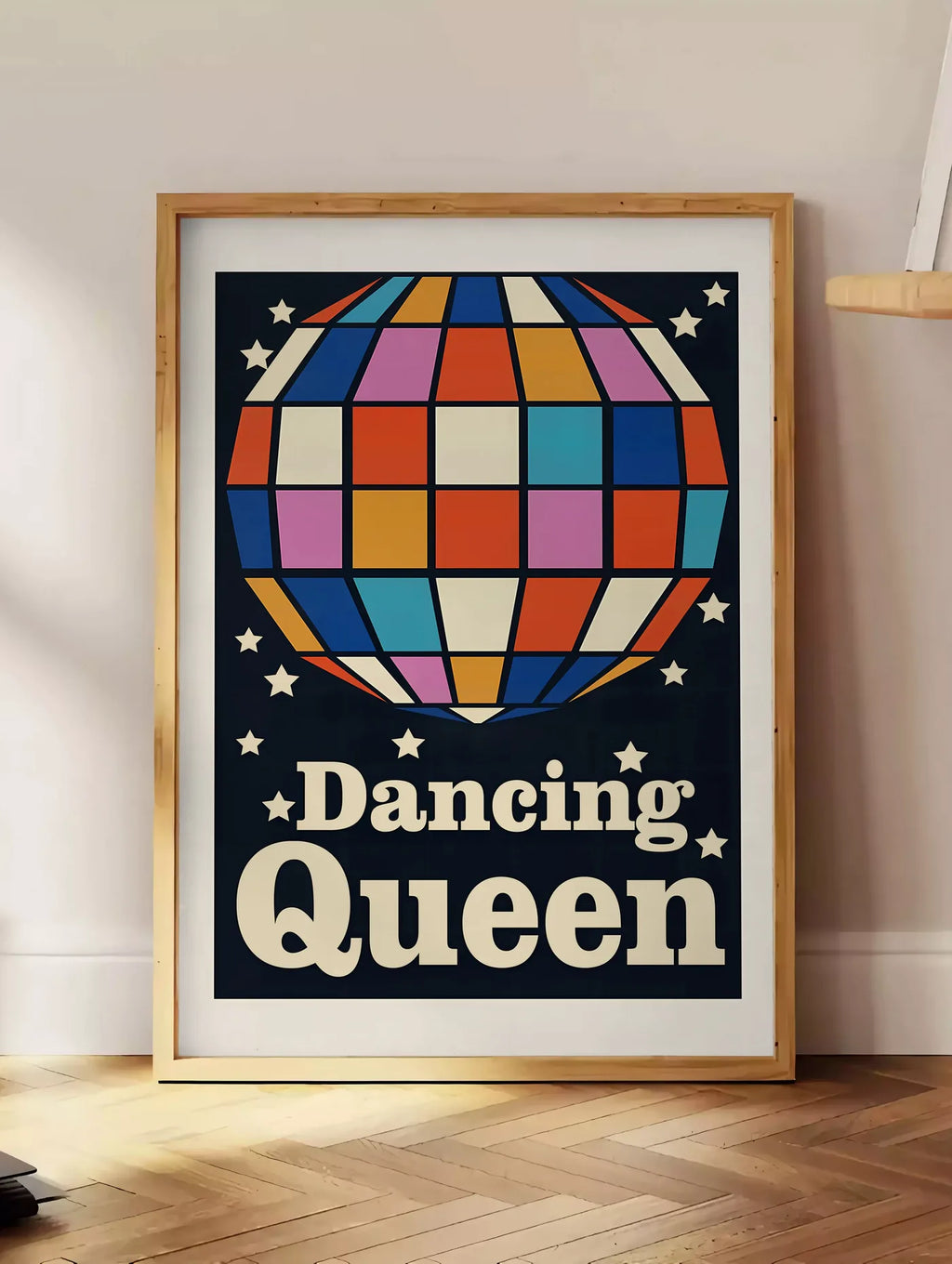 Estampe affiche vintage Dancing Queen, posee au sol dans un coin salon, sur un parquet a chevrons, pres d'une table d'appoint en chene chargee de livres