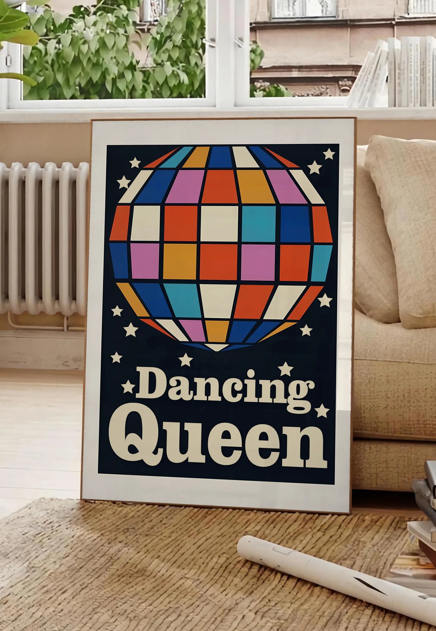 Poster affiche vintage Dancing Queen, posee au sol dans un salon parisien, devant une grande fenetre donnant sur un immeuble haussmannien, entre un ficus et un canape creme