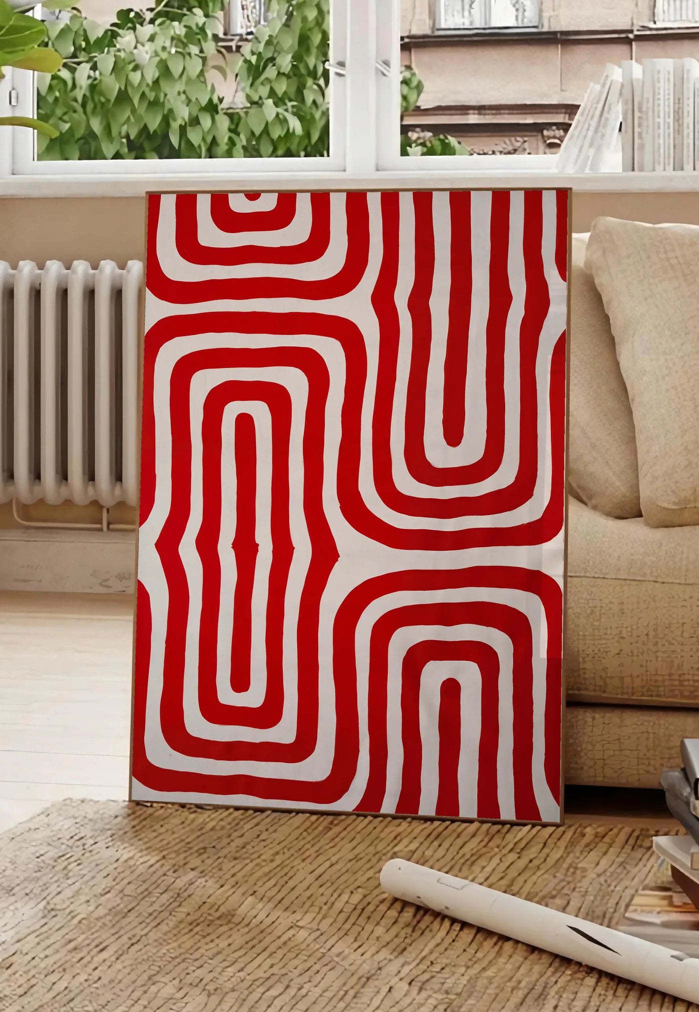 Poster labyrinthe de lignes rouges ondulees sur fond creme, posee au sol dans un salon parisien, devant une grande fenetre donnant sur un immeuble haussmannien, entre un ficus et un canape creme