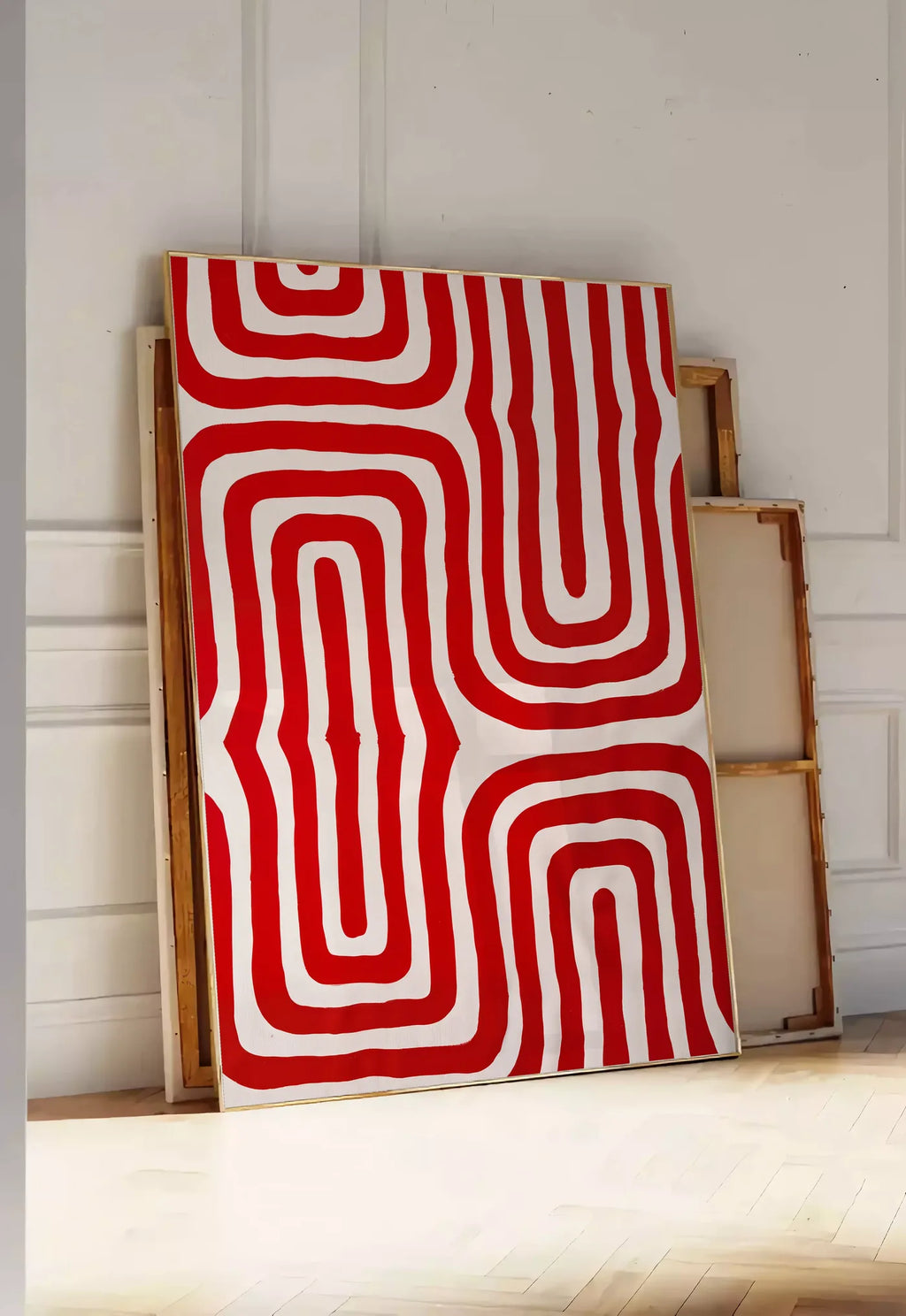 Tirage encadrable labyrinthe de lignes rouges ondulees sur fond creme, posee au sol dans une entree lumineuse, contre un mur a panneaux blancs, a cote de chassis en bois empiles