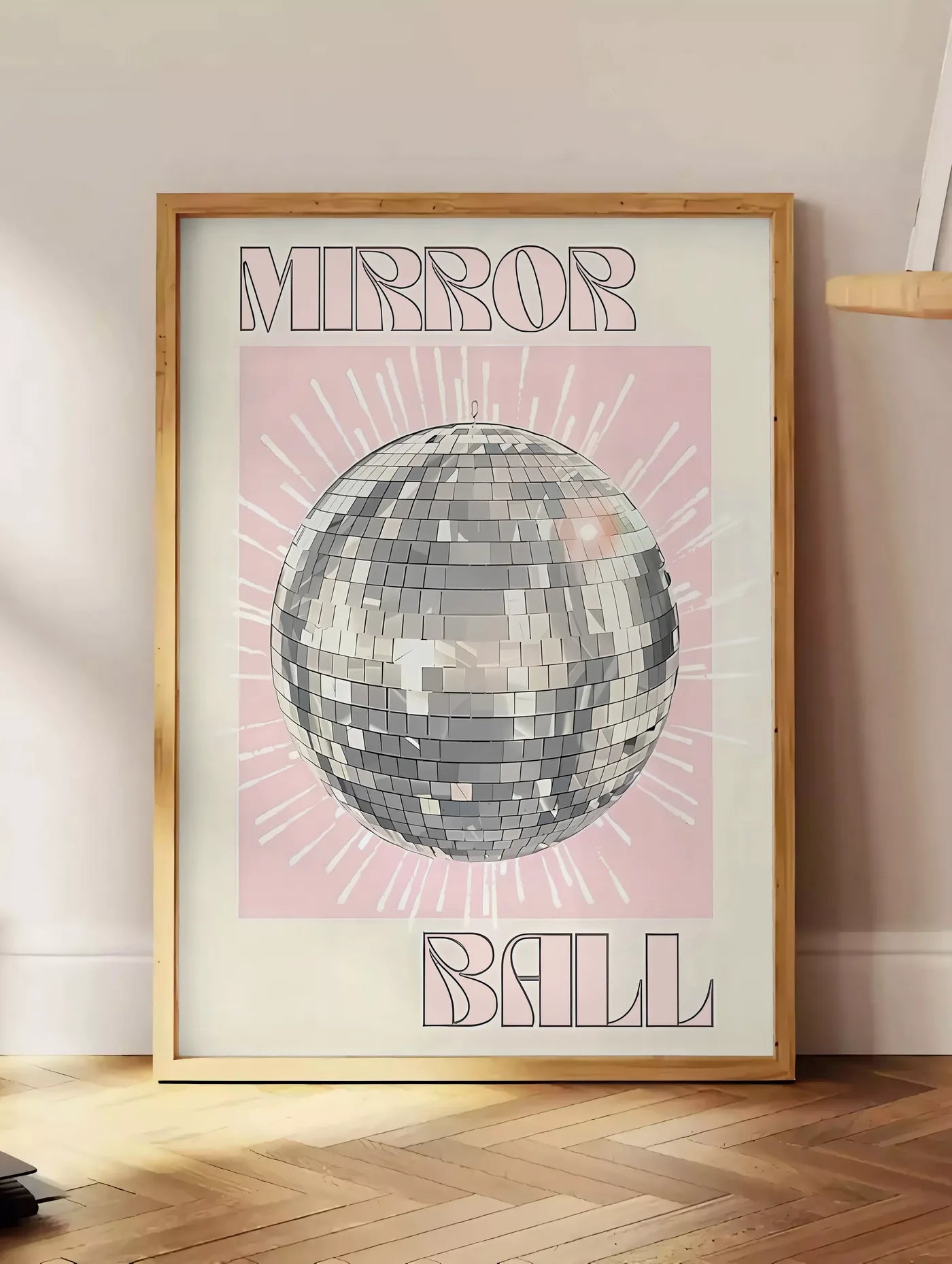 Estampe affiche vintage Mirror Ball, posee au sol dans un coin salon, sur un parquet a chevrons, pres d'une table d'appoint en chene chargee de livres
