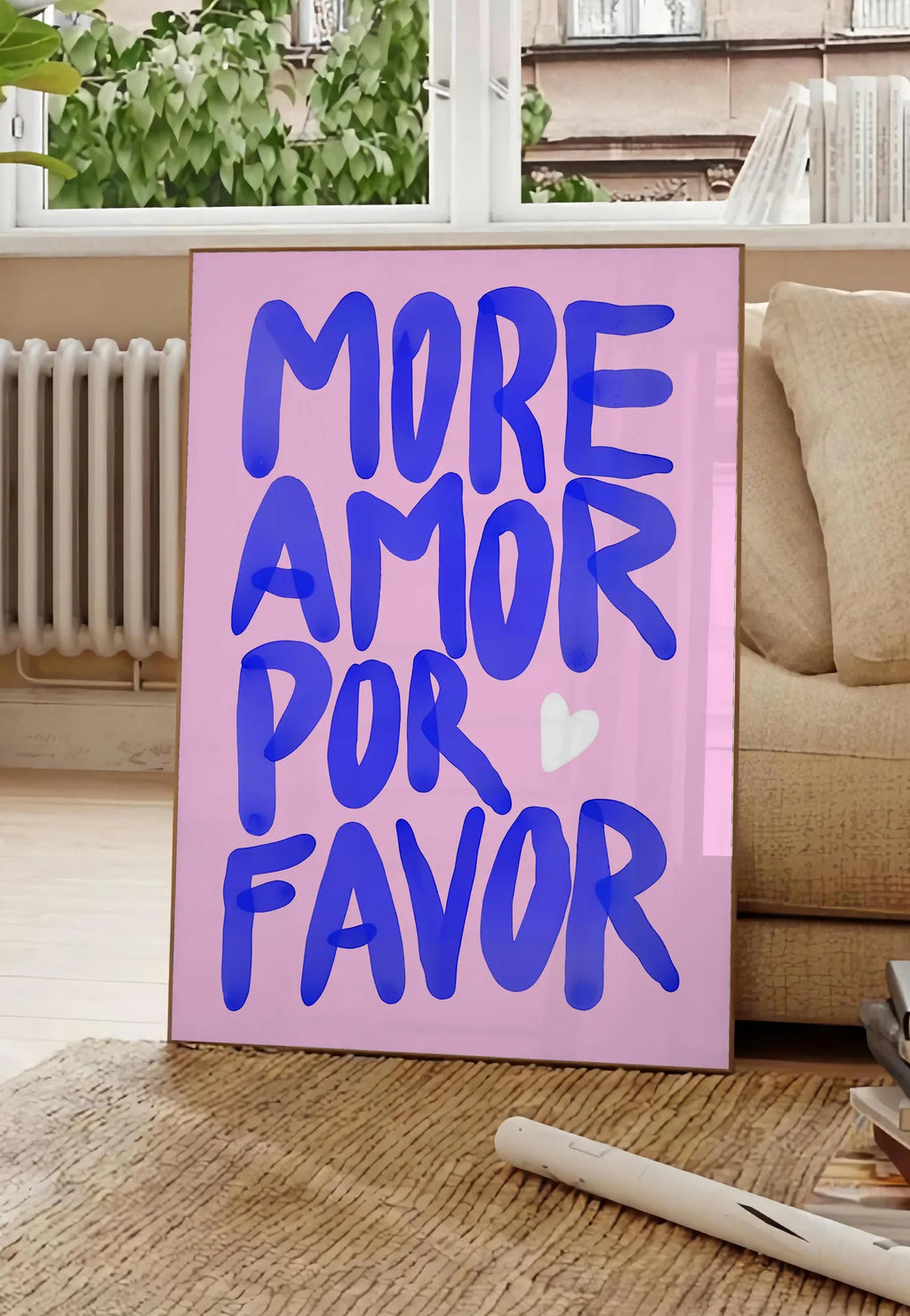 Poster affiche vintage More Amor Por Favor, posee au sol dans un salon parisien, devant une grande fenetre donnant sur un immeuble haussmannien, entre un ficus et un canape creme