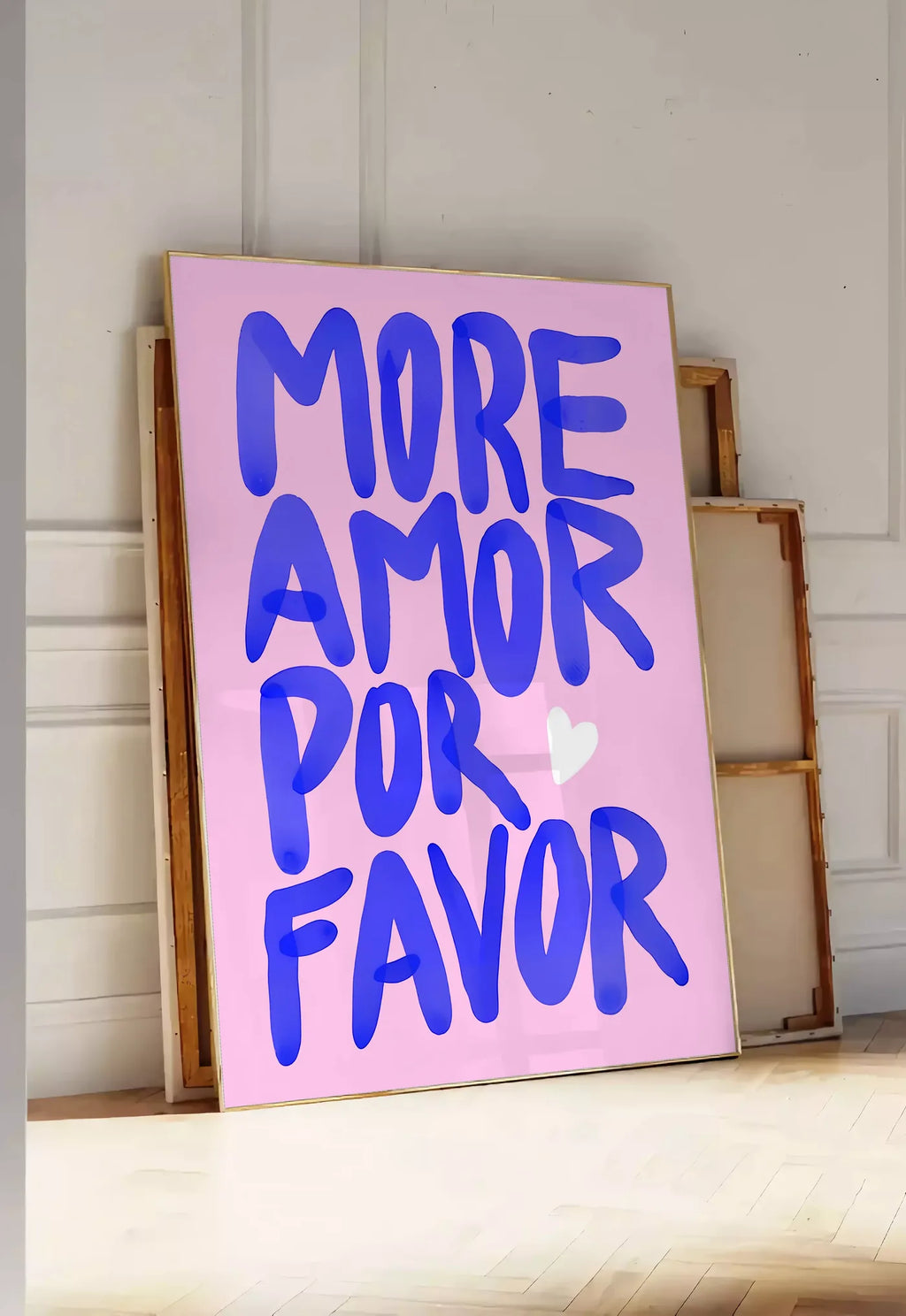 Tirage encadrable affiche vintage More Amor Por Favor, posee au sol dans une entree lumineuse, contre un mur a panneaux blancs, a cote de chassis en bois empiles
