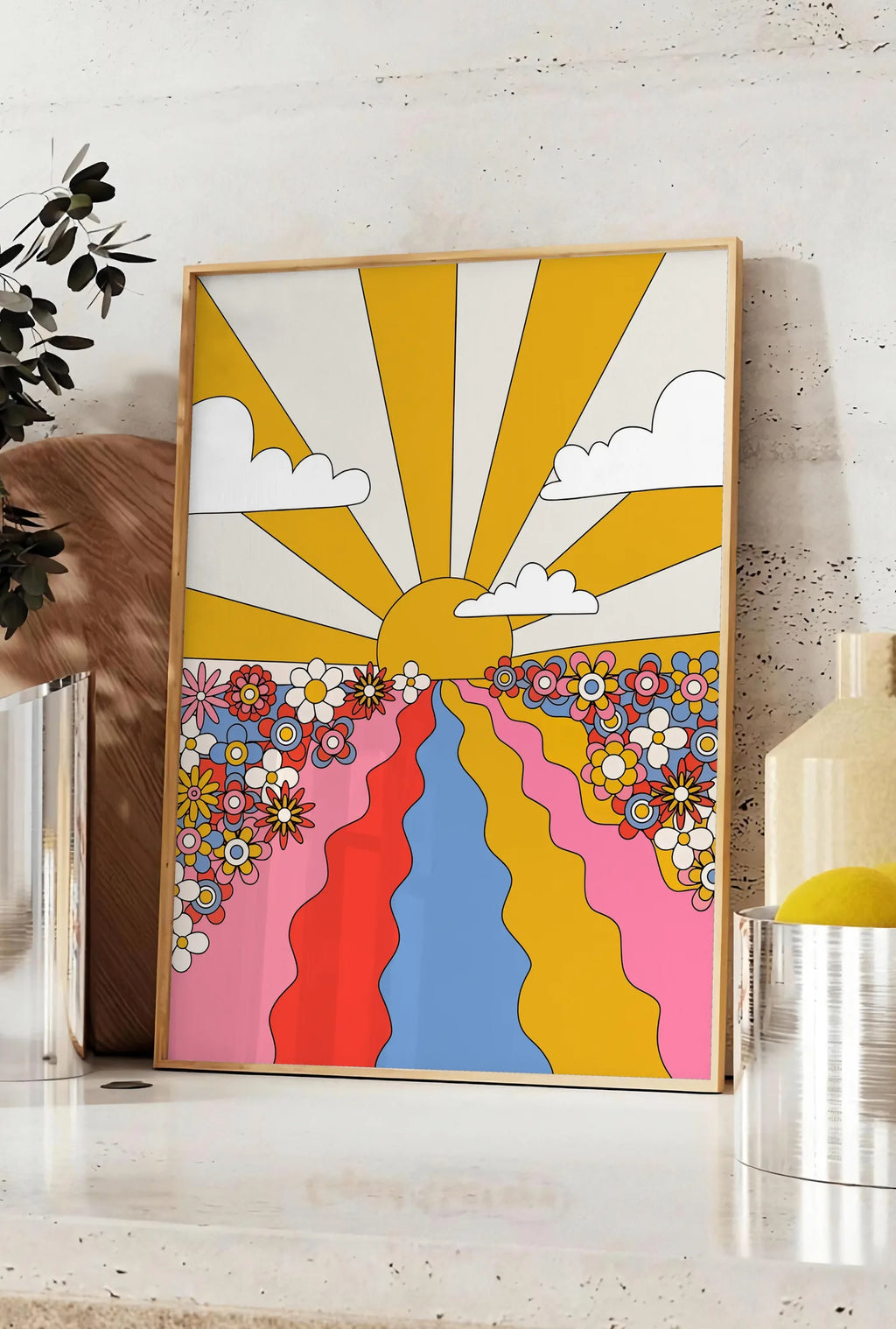 Affiche soleil aux rayons jaunes fleurs et chemin ondule, posee sur un plan de travail de cuisine en pierre claire, entre une branche d'eucalyptus en vase et un bocal de citrons