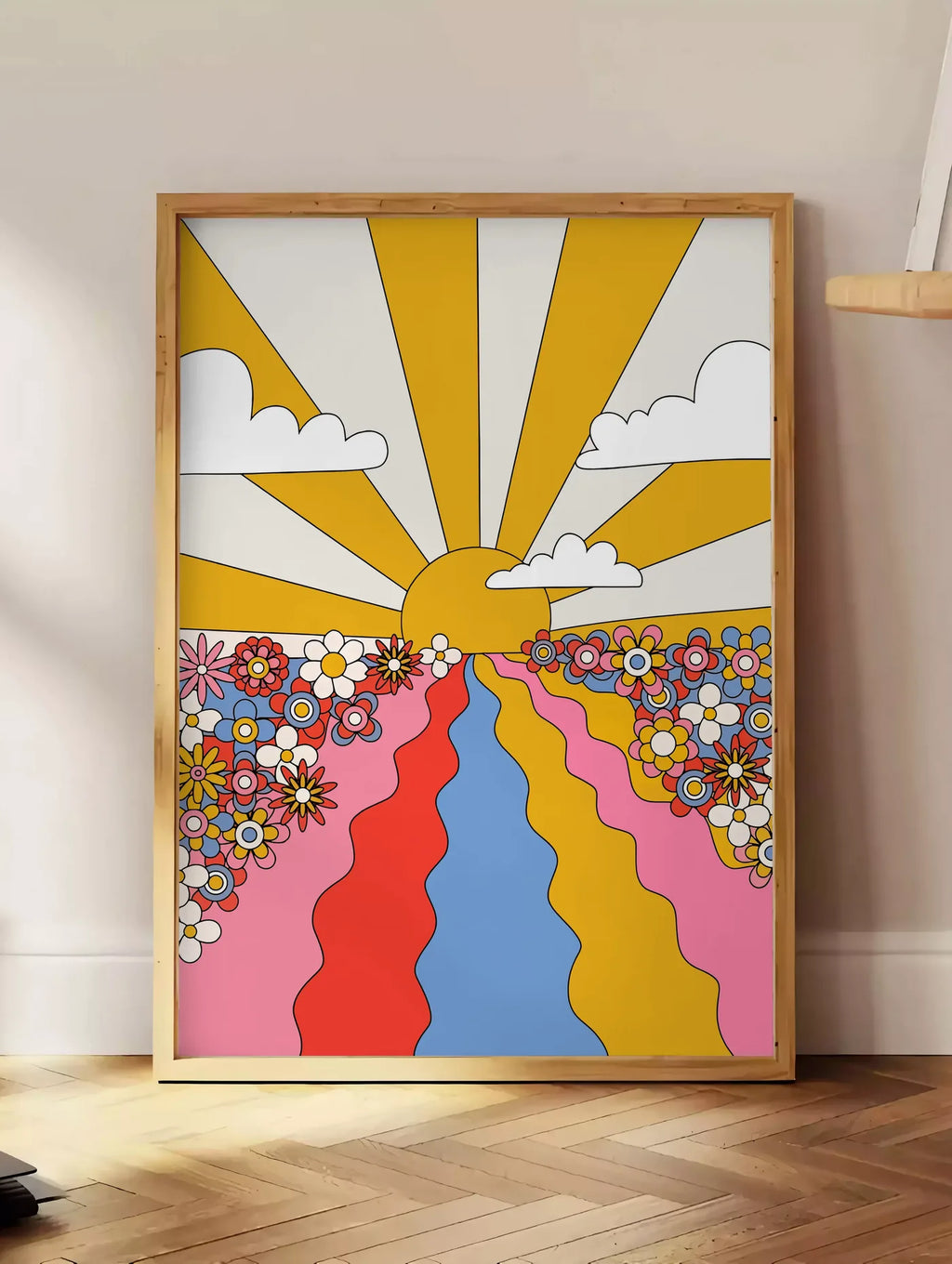 Estampe soleil aux rayons jaunes fleurs et chemin ondule, posee au sol dans un coin salon, sur un parquet a chevrons, pres d'une table d'appoint en chene chargee de livres