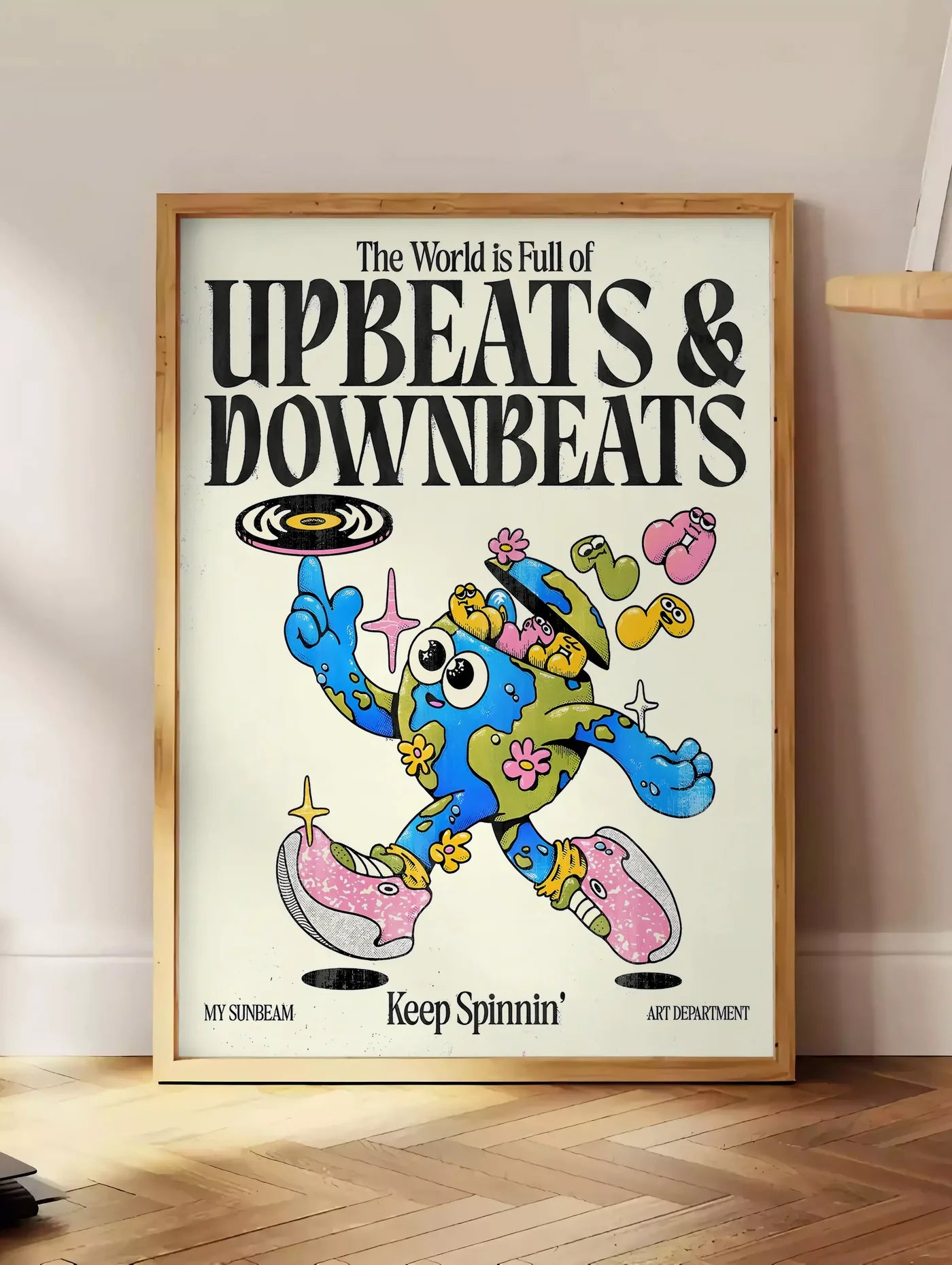 Estampe affiche vintage Upbeats and Downbeats, posee au sol dans un coin salon, sur un parquet a chevrons, pres d'une table d'appoint en chene chargee de livres