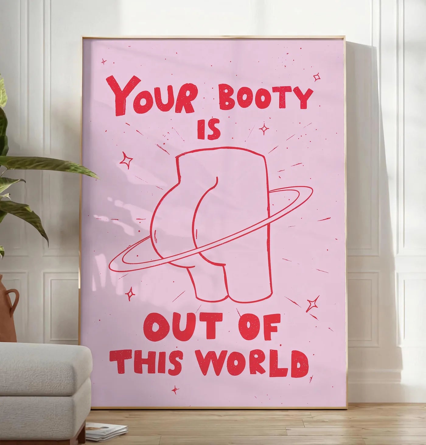 Reproduction affiche vintage Your Booty, posee au sol dans un salon minimaliste clair, a cote d'un canape beige et d'une plante verte, sur un parquet clair