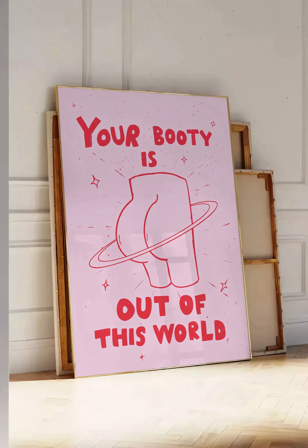 Tirage encadrable affiche vintage Your Booty, posee au sol dans une entree lumineuse, contre un mur a panneaux blancs, a cote de chassis en bois empiles