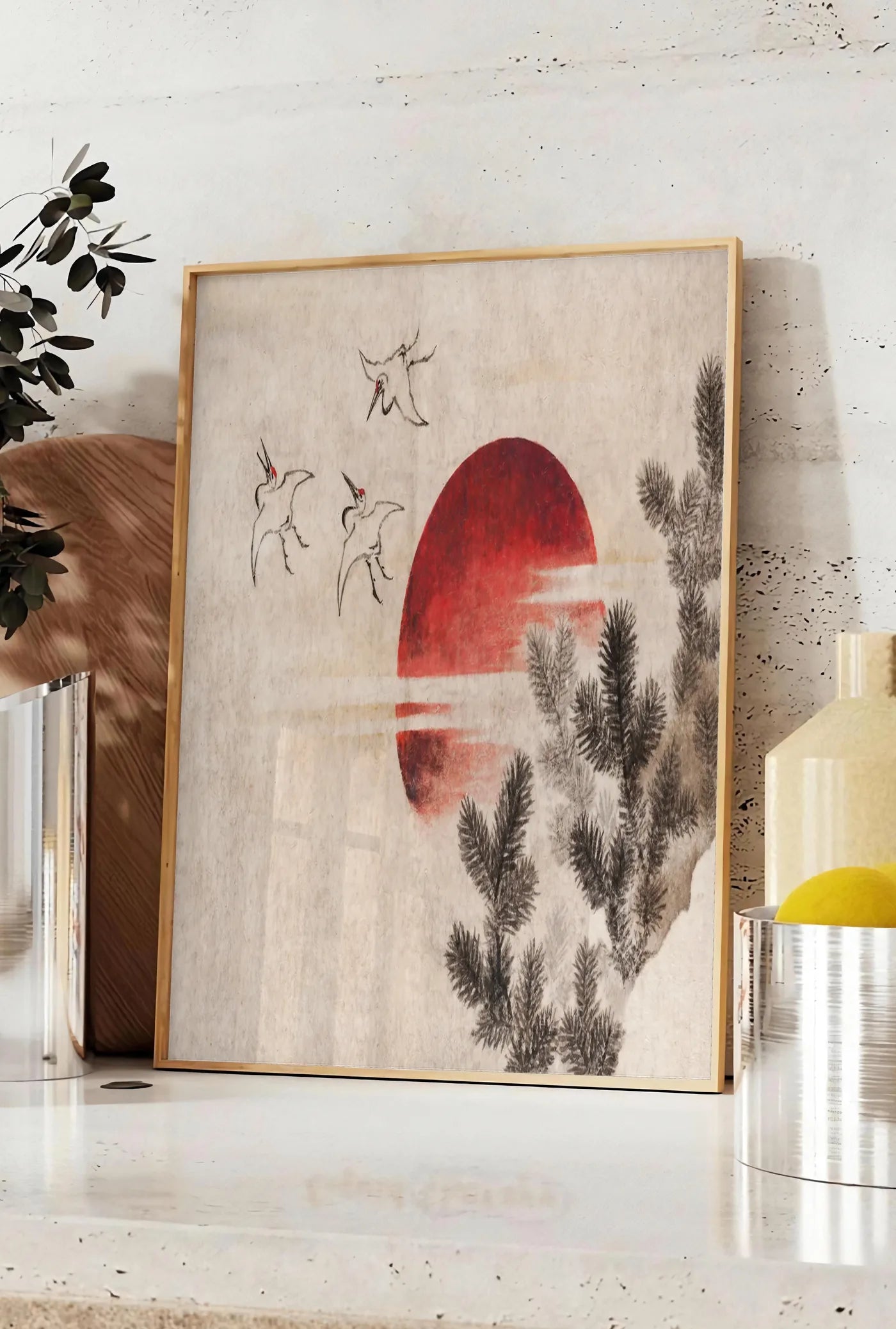 Affiche affiche grues et soleil rouge art japonais, posee sur un plan de travail de cuisine en pierre claire, entre une branche d'eucalyptus en vase et un bocal de citrons