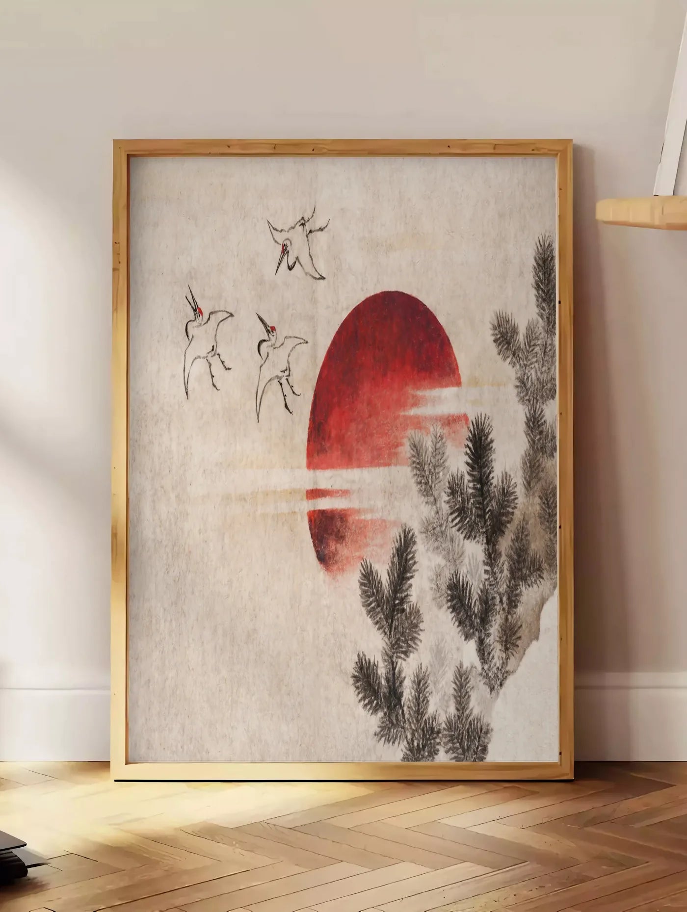 Estampe affiche grues et soleil rouge art japonais, posee au sol dans un coin salon, sur un parquet a chevrons, pres d'une table d'appoint en chene chargee de livres