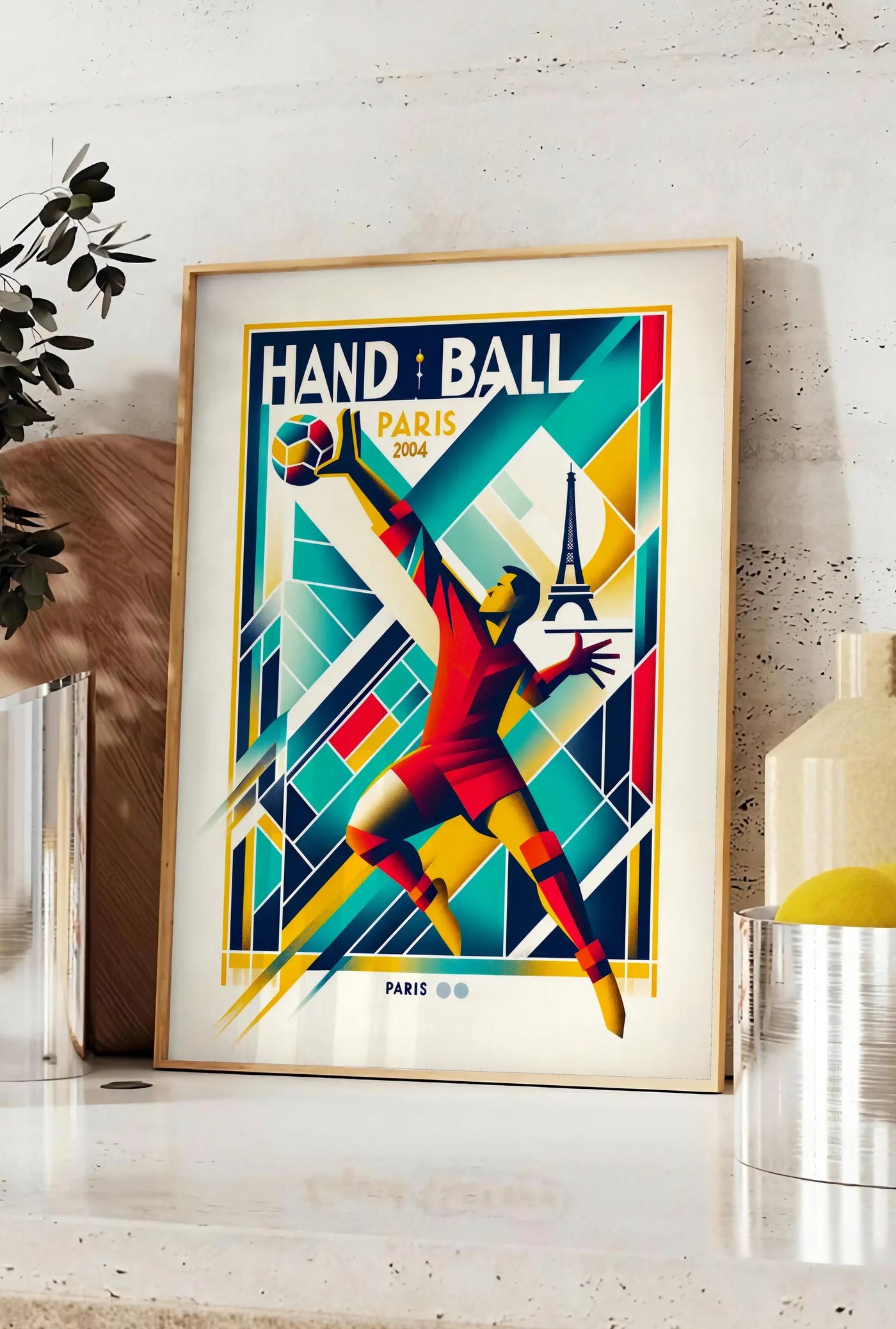 Affiche stylisé joueur de handball en saut, posee sur un plan de travail de cuisine en pierre claire, entre une branche d'eucalyptus en vase et un bocal de citrons