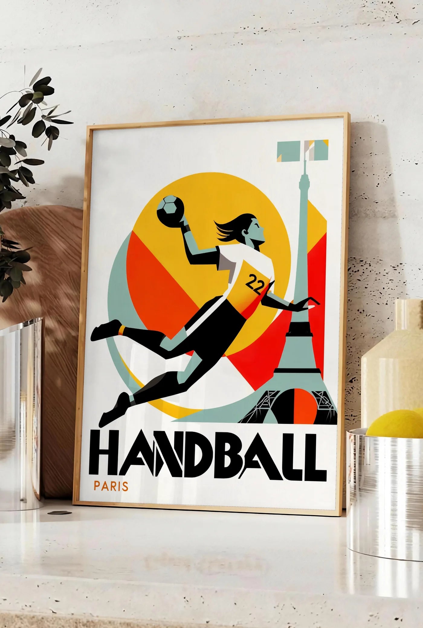 Affiche affiche handball Paris, posee sur un plan de travail de cuisine en pierre claire, entre une branche d'eucalyptus en vase et un bocal de citrons