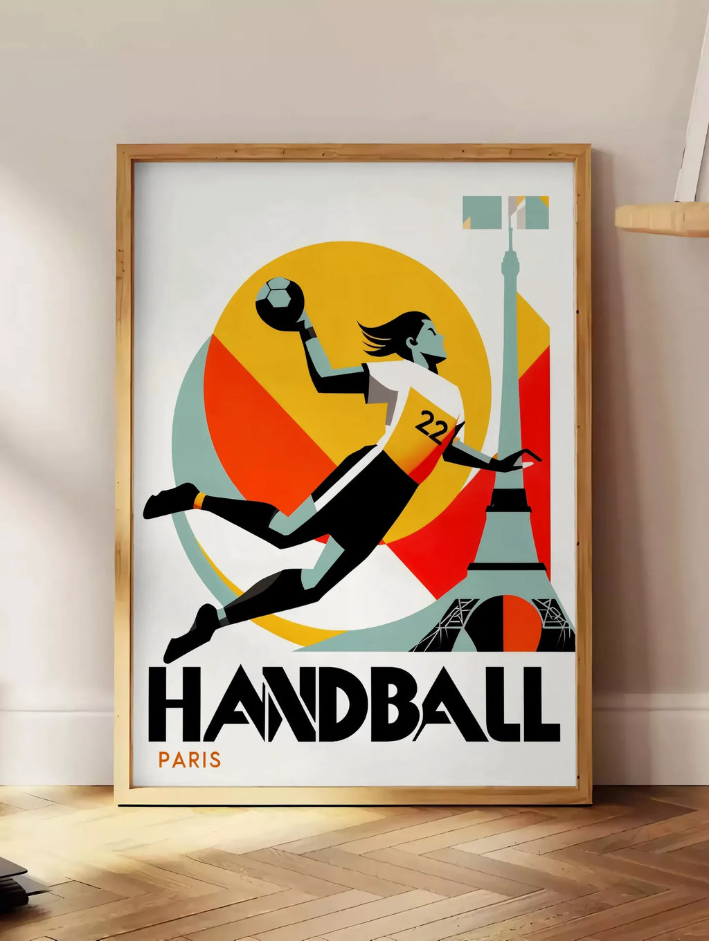Estampe affiche handball Paris, posee au sol dans un coin salon, sur un parquet a chevrons, pres d'une table d'appoint en chene chargee de livres