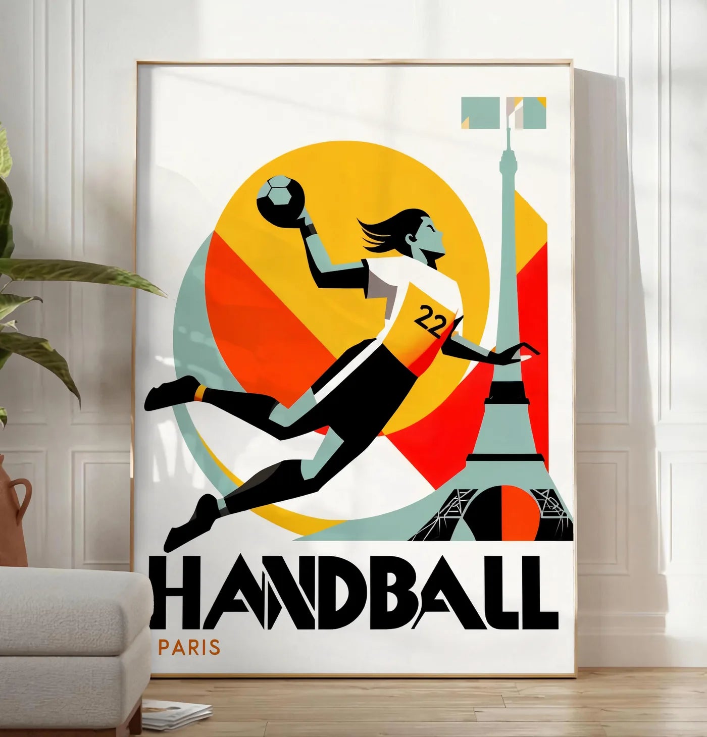 Reproduction affiche handball Paris, posee au sol dans un salon minimaliste clair, a cote d'un canape beige et d'une plante verte, sur un parquet clair