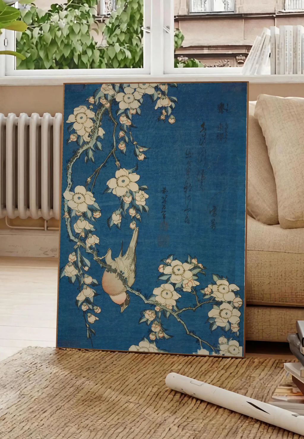 Poster affiche Hokusai bouvreuil sur cerisier, posee au sol dans un salon parisien, devant une grande fenetre donnant sur un immeuble haussmannien, entre un ficus et un canape creme