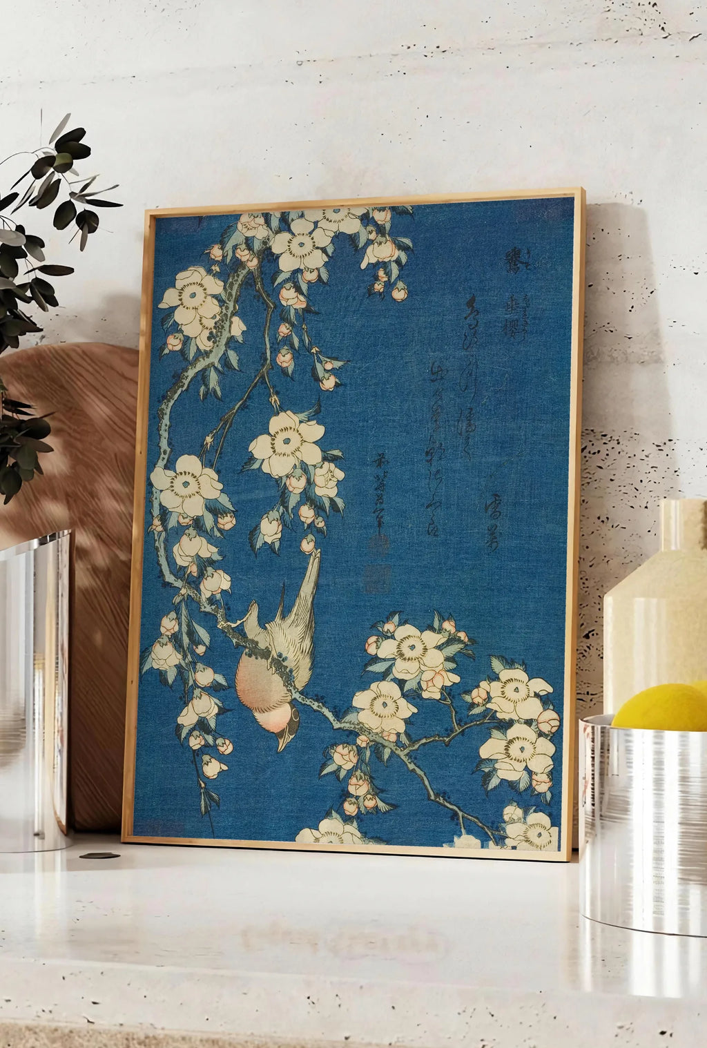 Affiche affiche Hokusai cerisier en fleurs et bouvreuil, posee sur un plan de travail de cuisine en pierre claire, entre une branche d'eucalyptus en vase et un bocal de citrons