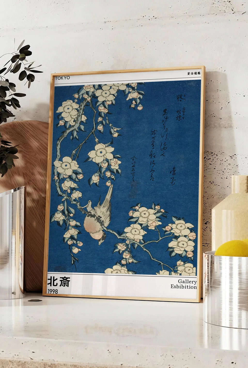 Affiche affiche Hokusai bouvreuil et cerisier, posee sur un plan de travail de cuisine en pierre claire, entre une branche d'eucalyptus en vase et un bocal de citrons