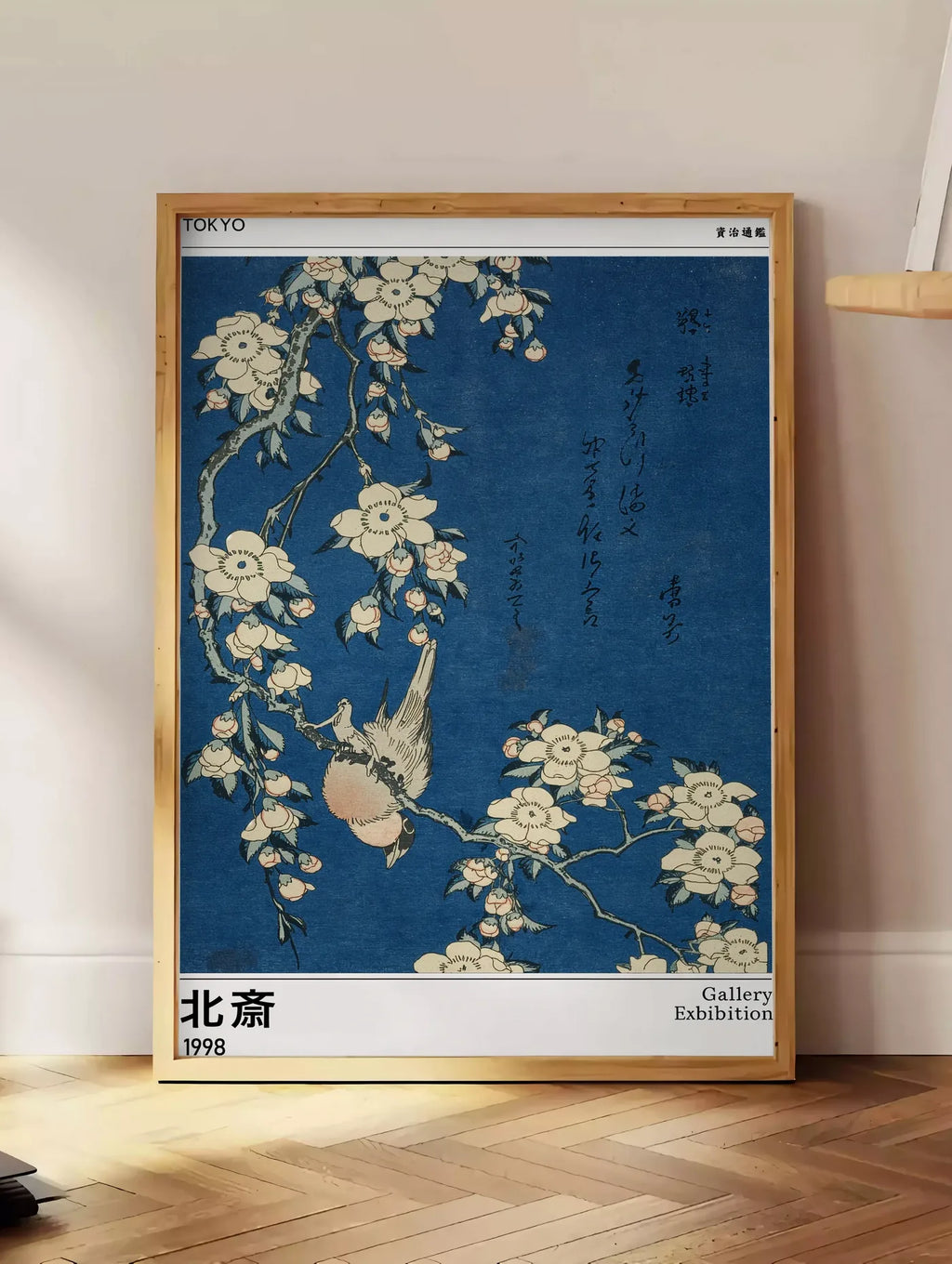 Estampe affiche Hokusai bouvreuil et cerisier, posee au sol dans un coin salon, sur un parquet a chevrons, pres d'une table d'appoint en chene chargee de livres